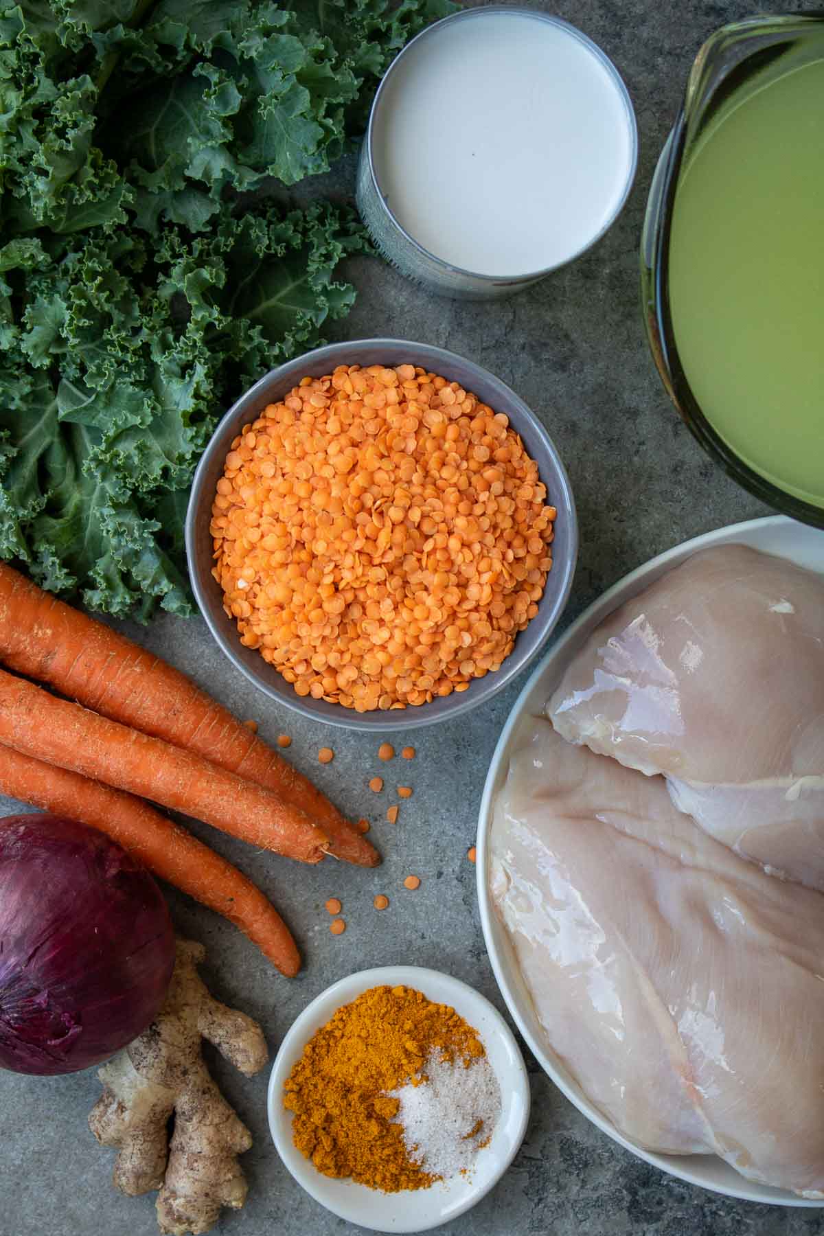 Ingredients for golden chicken lentil soup: red lentils, coconut milk, broth, chicken breasts, curry powder, turmeric, salt, ginger, garlic, onion, carrots, and kale.
