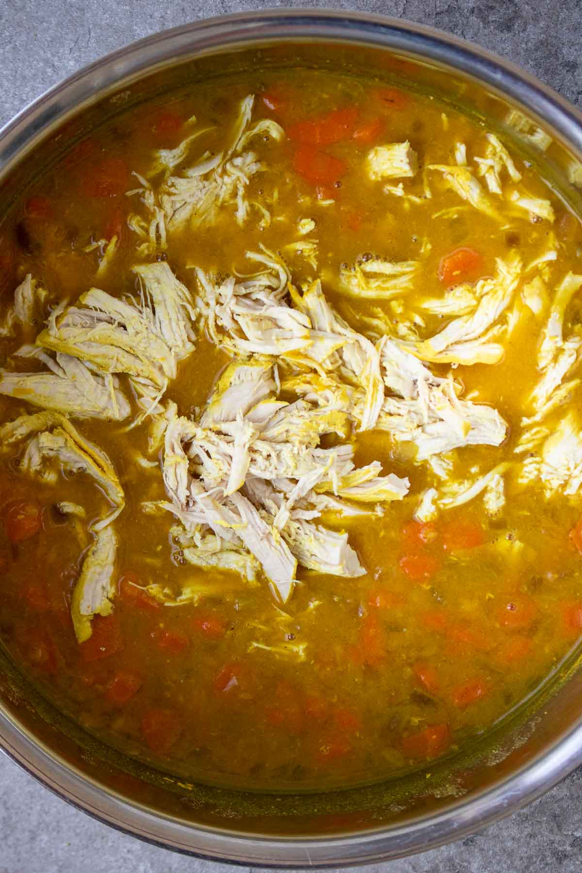 Large pot with cooked lentil soup with shredded chicken on top.