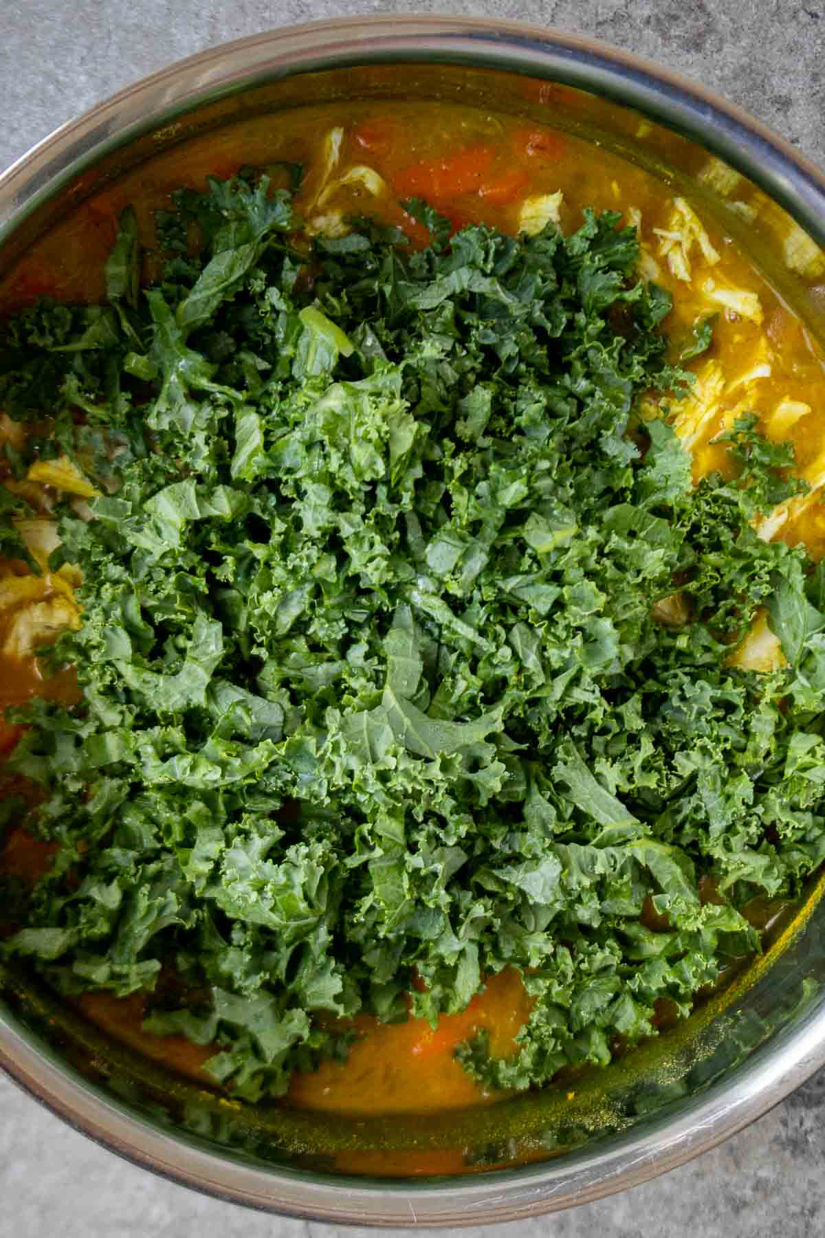 Chicken and lentil soup in a large pot with chopped kale on top.