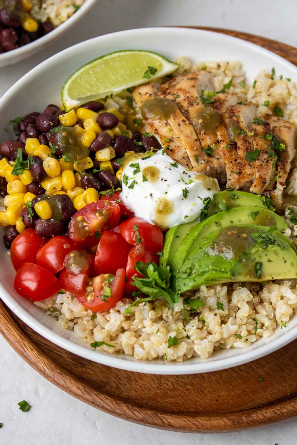 Overhead view of bowl with grains, grilled chicken, black bean and corn salsa, cherry tomatoes, avocado, Greek yogurt, salsa verde, and fresh cilantro.