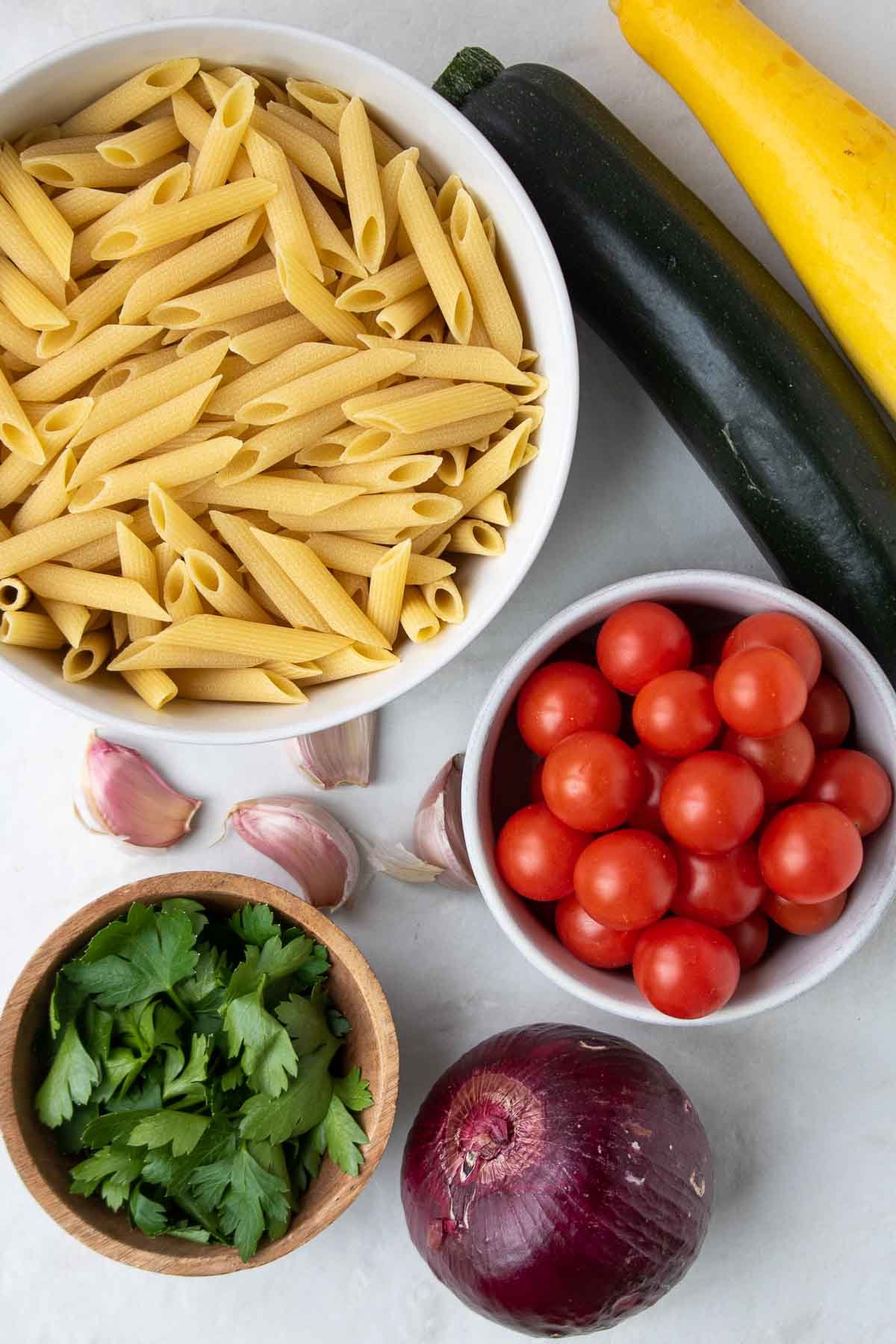 Ingrédients pour les pâtes au poulet et aux légumes : pâtes penne, courgettes vertes, courgettes jaunes, tomates cerises, ail, oignon rouge, persil.