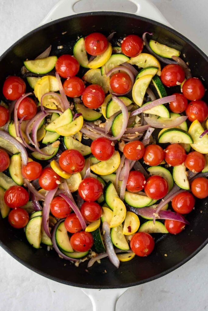 Cooked zucchini, cherry, tomatoes, and red onion in a cast iron skillet.