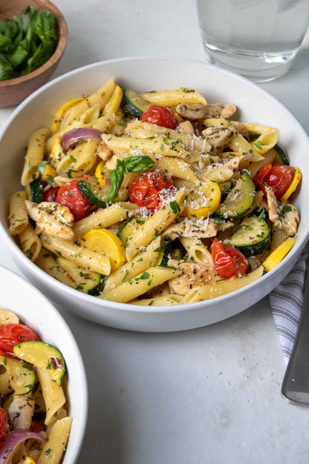 Two bowls of pasta with chicken and vegetables with a fork and napkin.