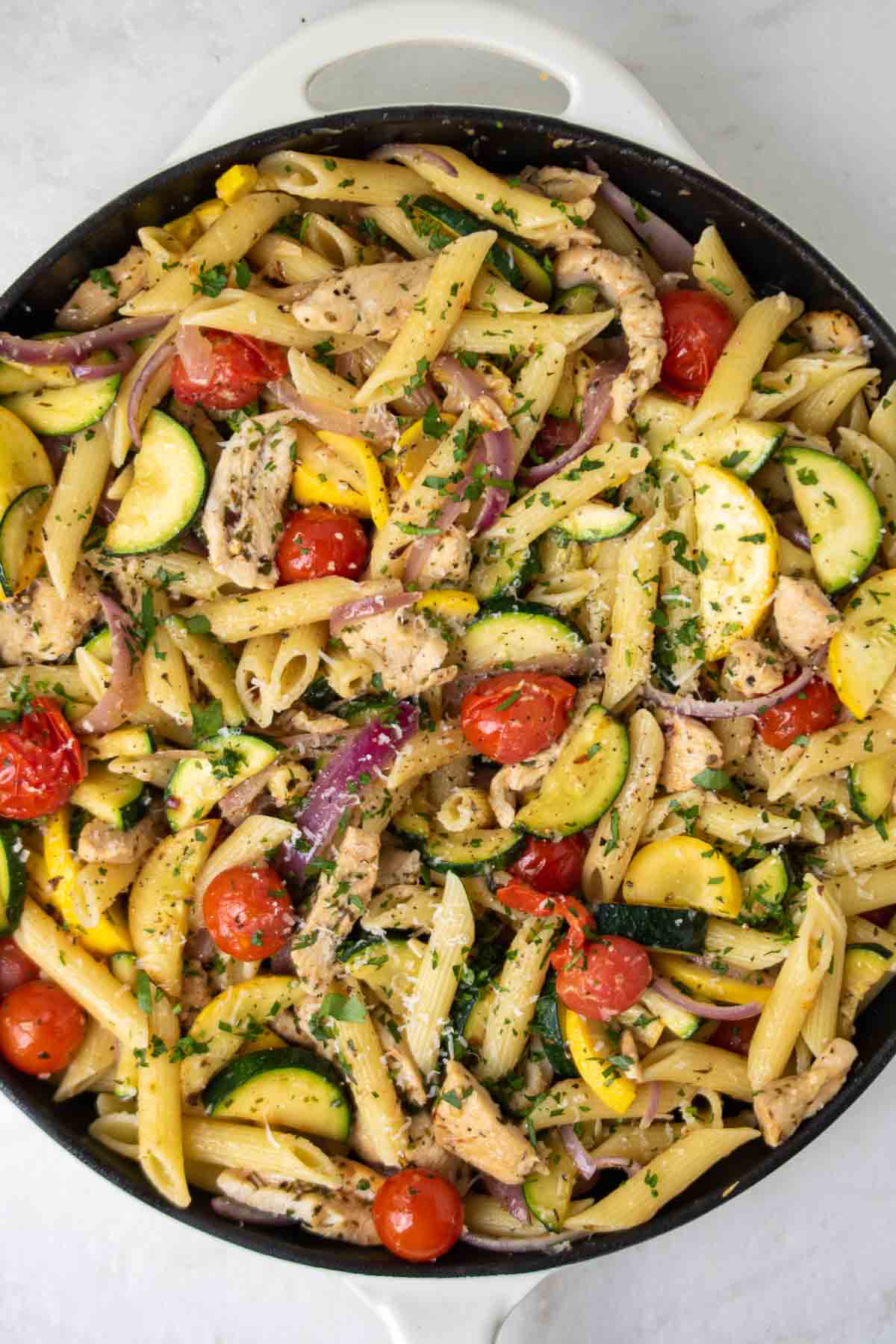 Pasta with chicken, zucchini, cherry tomatoes, red onion, and herbs in a cast iron skillet.