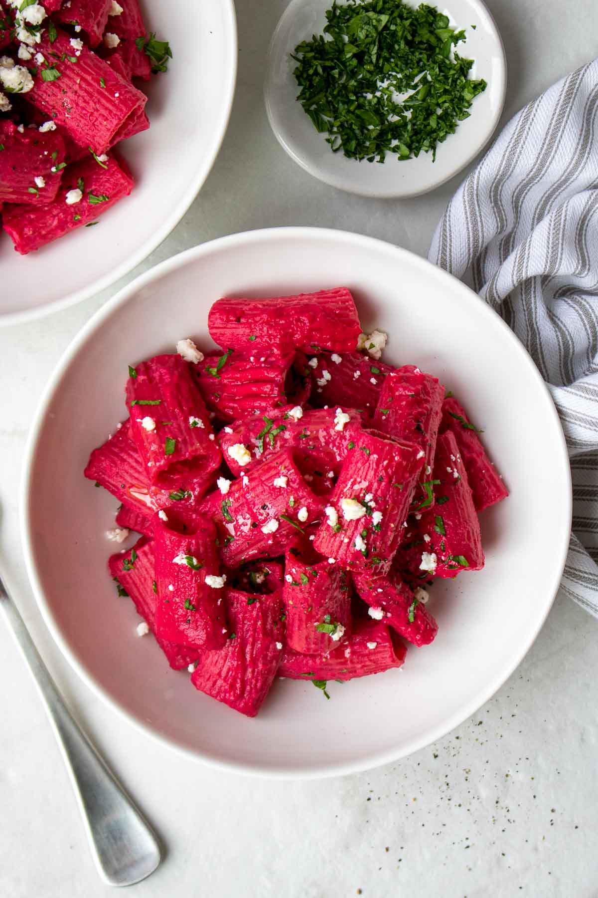 Roasted beet pasta with feta and parsley in a white bowl with a fork and tea towel.
