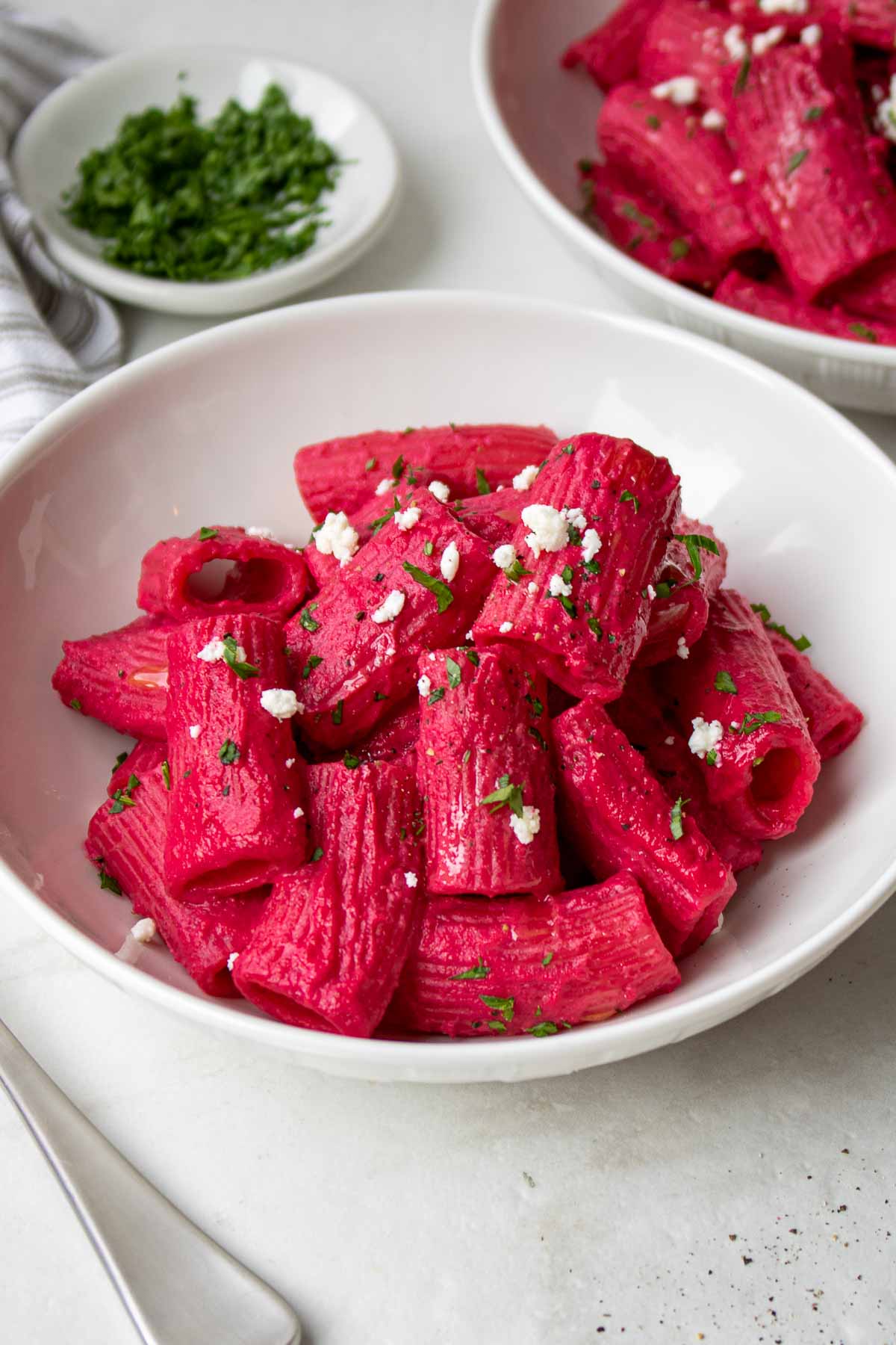 Beet pasta with feta cheese and parsley on top in a white bowl.