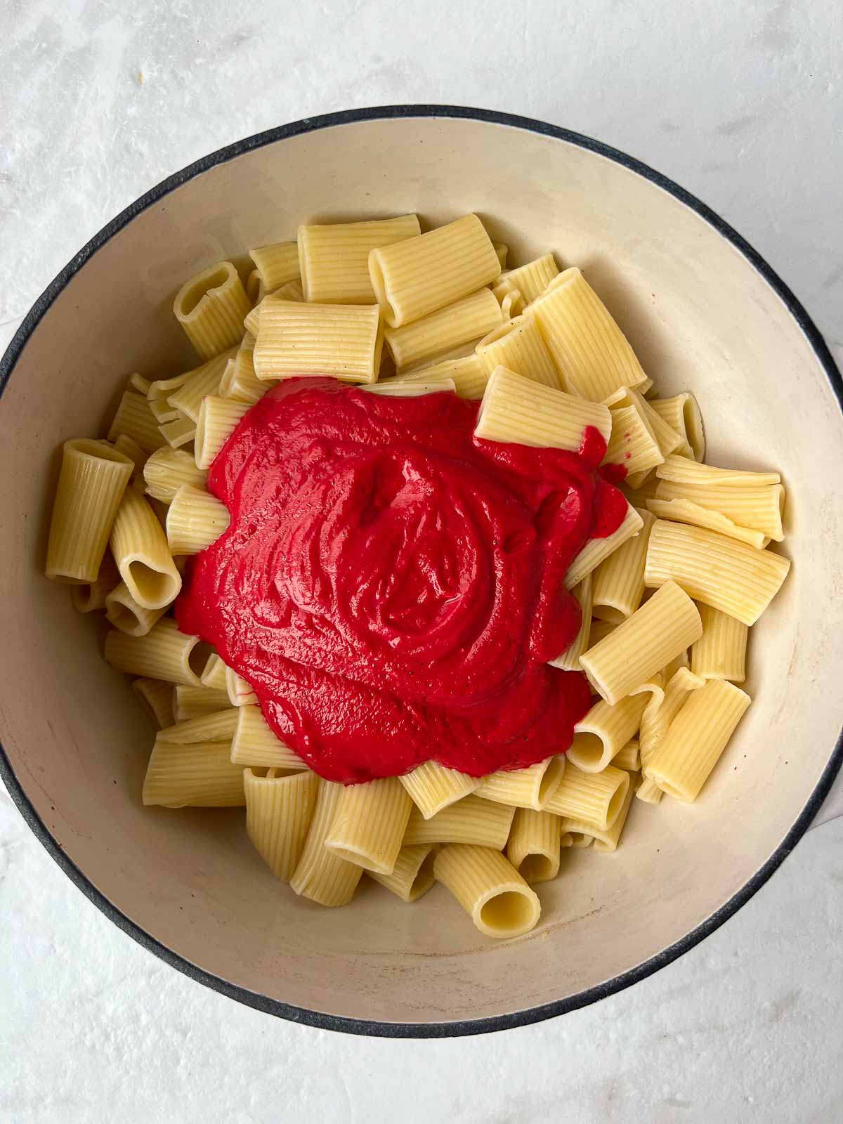 Cooked pasta with beet pasta sauce in a pot.