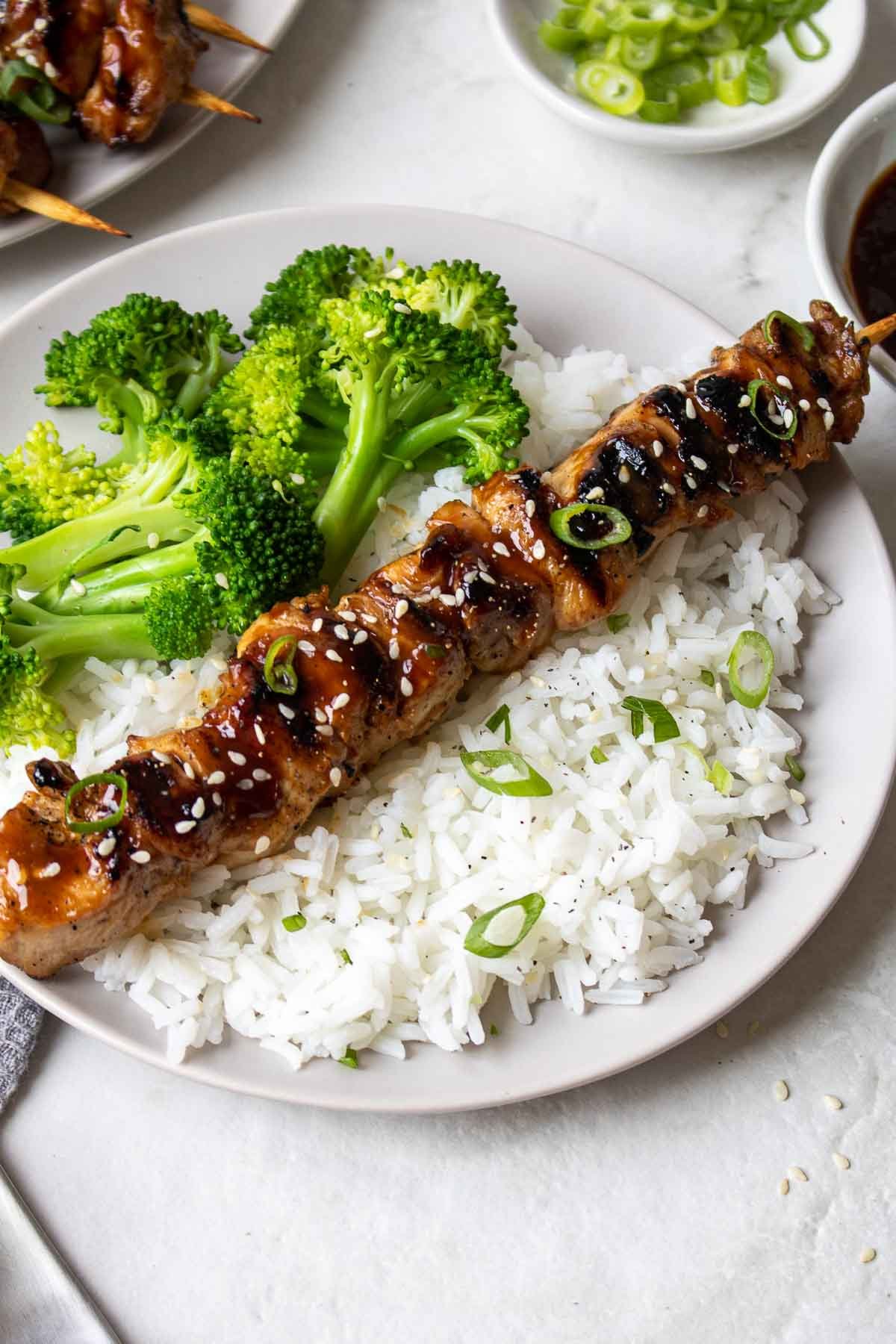 Grilled teriyaki chicken skewer on a plate with rice and broccoli.