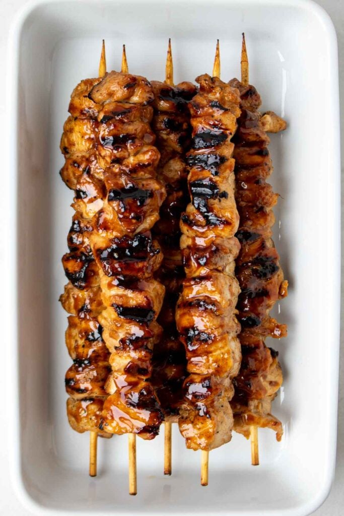 Grilled teriyaki chicken skewers in a white dish.