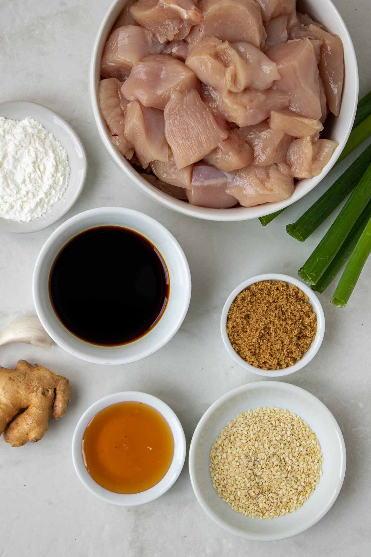 Ingredients for teriyaki chicken skewers: cubed chicken, soy sauce, brown sugar, honey, ginger, garlic, cornstarch, sesame seeds, and green onions.