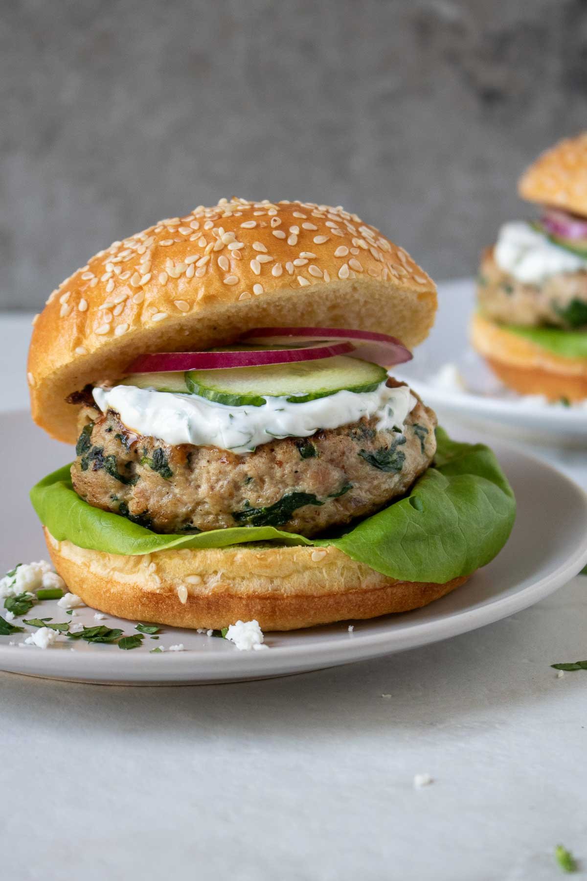A spinach feta turkey burger on a bun with yogurt sauce, cucumber, lettuce, red onion, and cucumber on a plate.