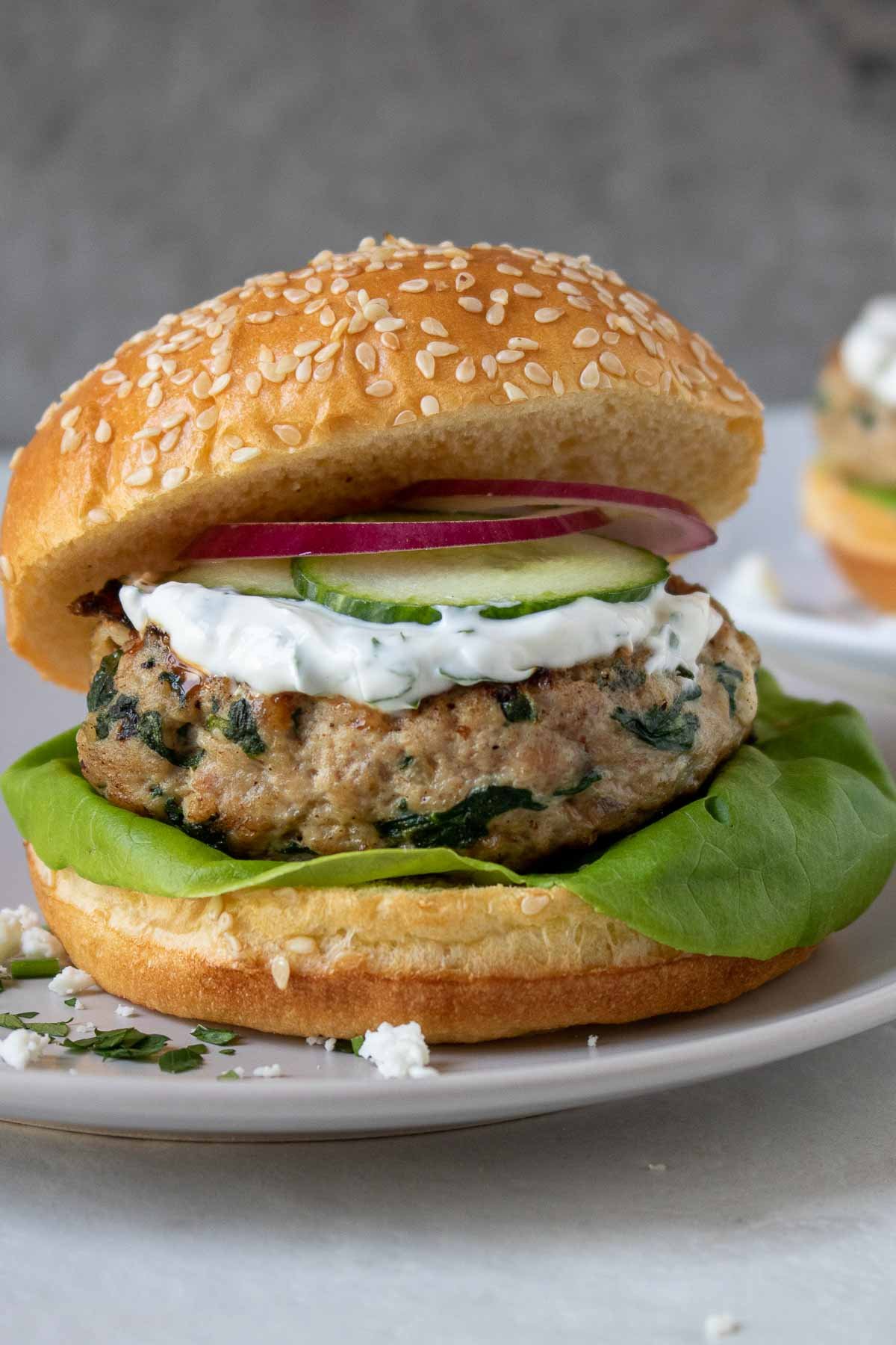 Close up of spinach feta turkey burgers on a plate with tzatziki-style sauce, red onion, cucumber, and lettuce.