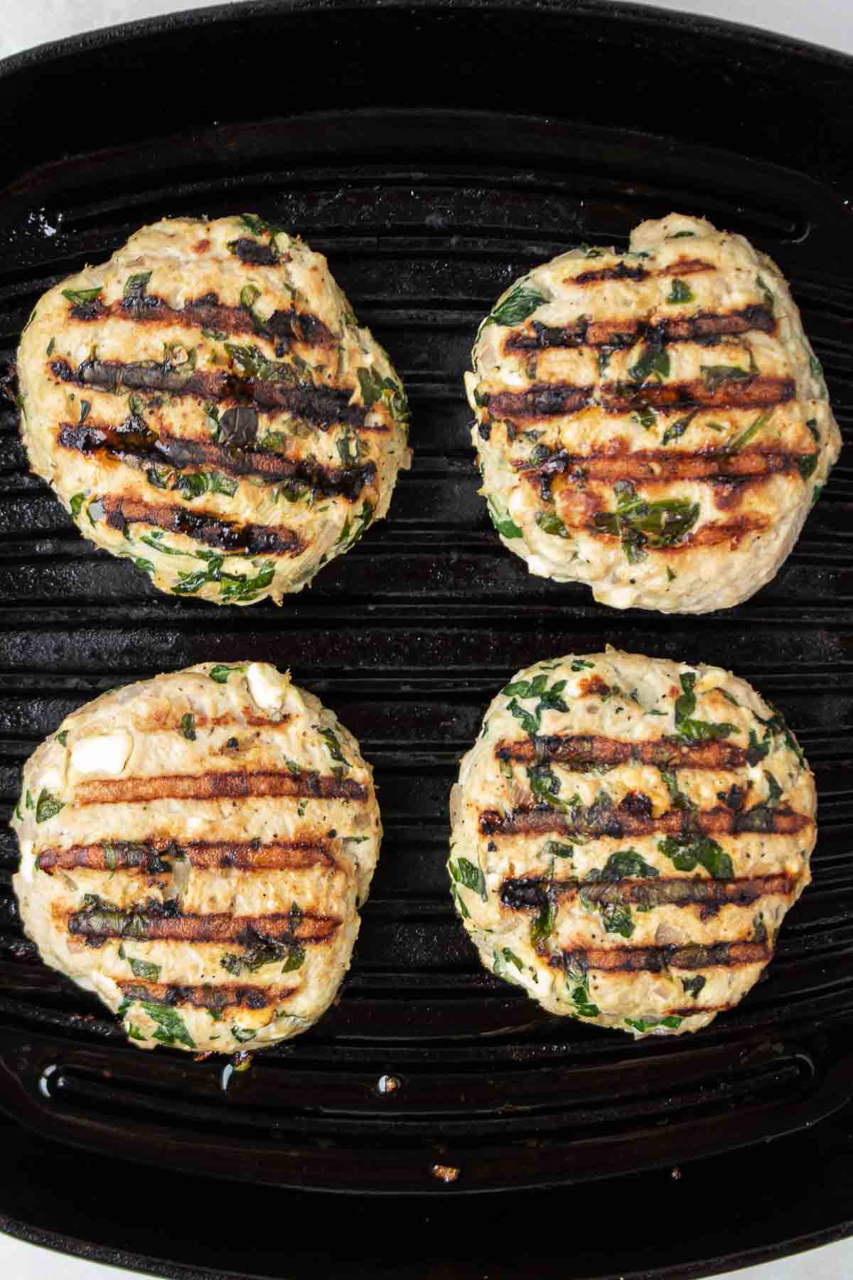 Spinach feta turkey burger patties cooking in a cast iron grill pan.