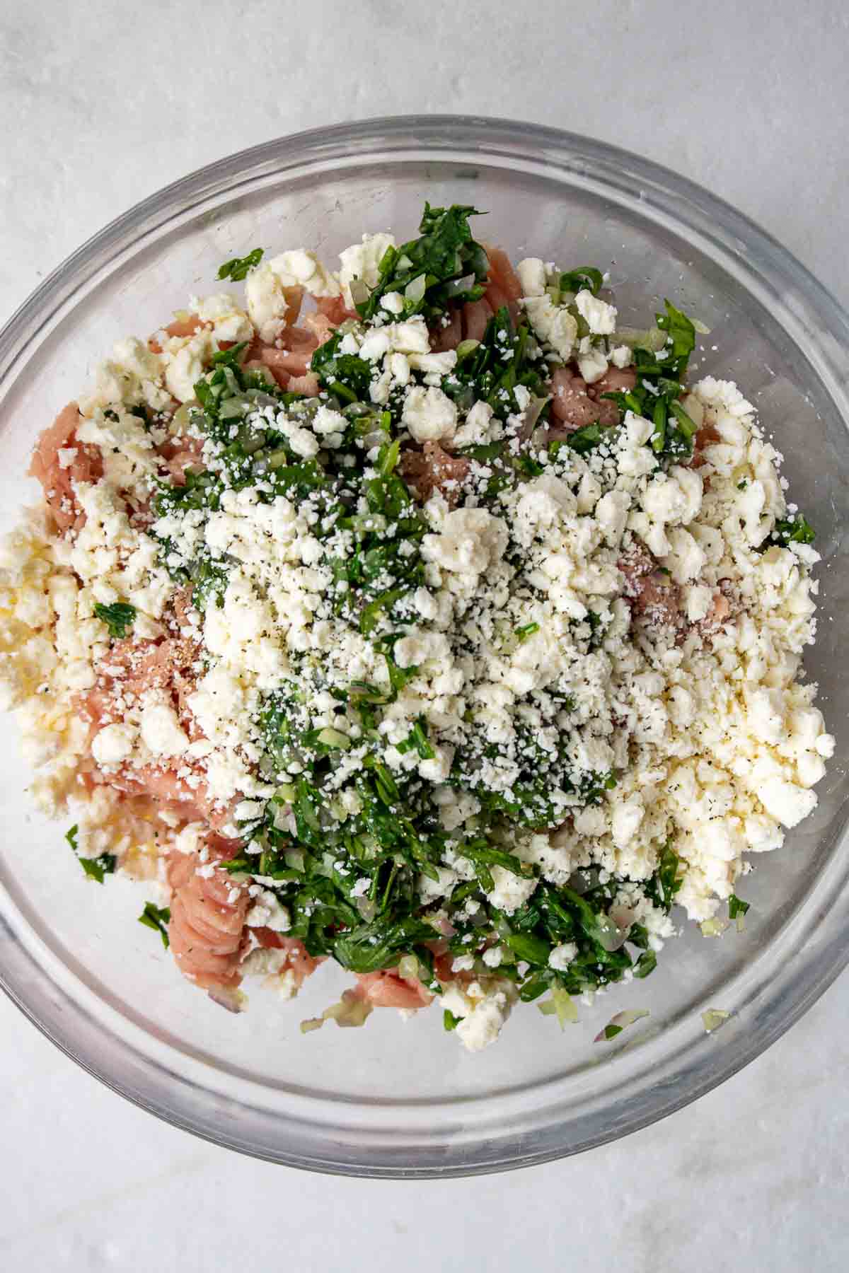 Ingredients for turkey burgers in a bowl; onion, garlic, ground turkey, cooked spinach, crumbled feta cheese, salt, and black pepper.