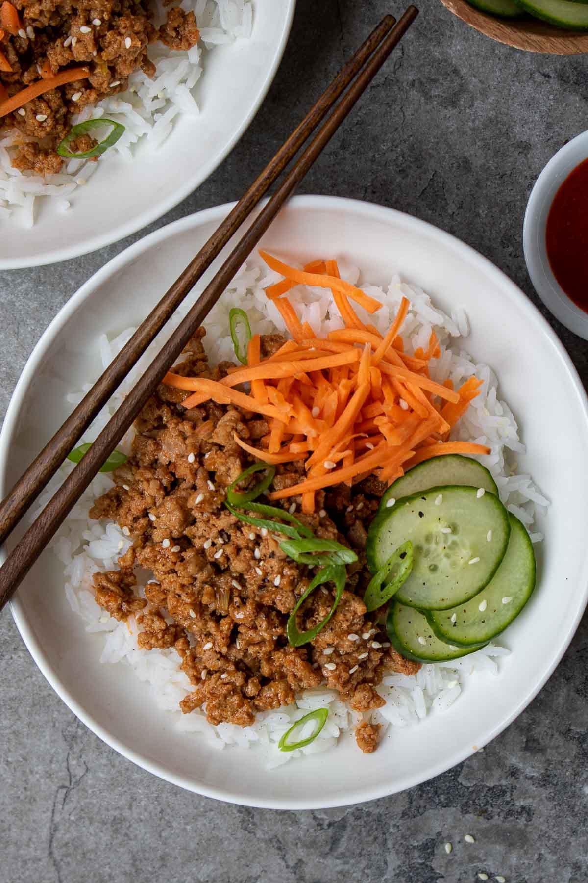 Closeup of Korean ground turkey and rice in white bowls with gochujang and cucumber on the side.