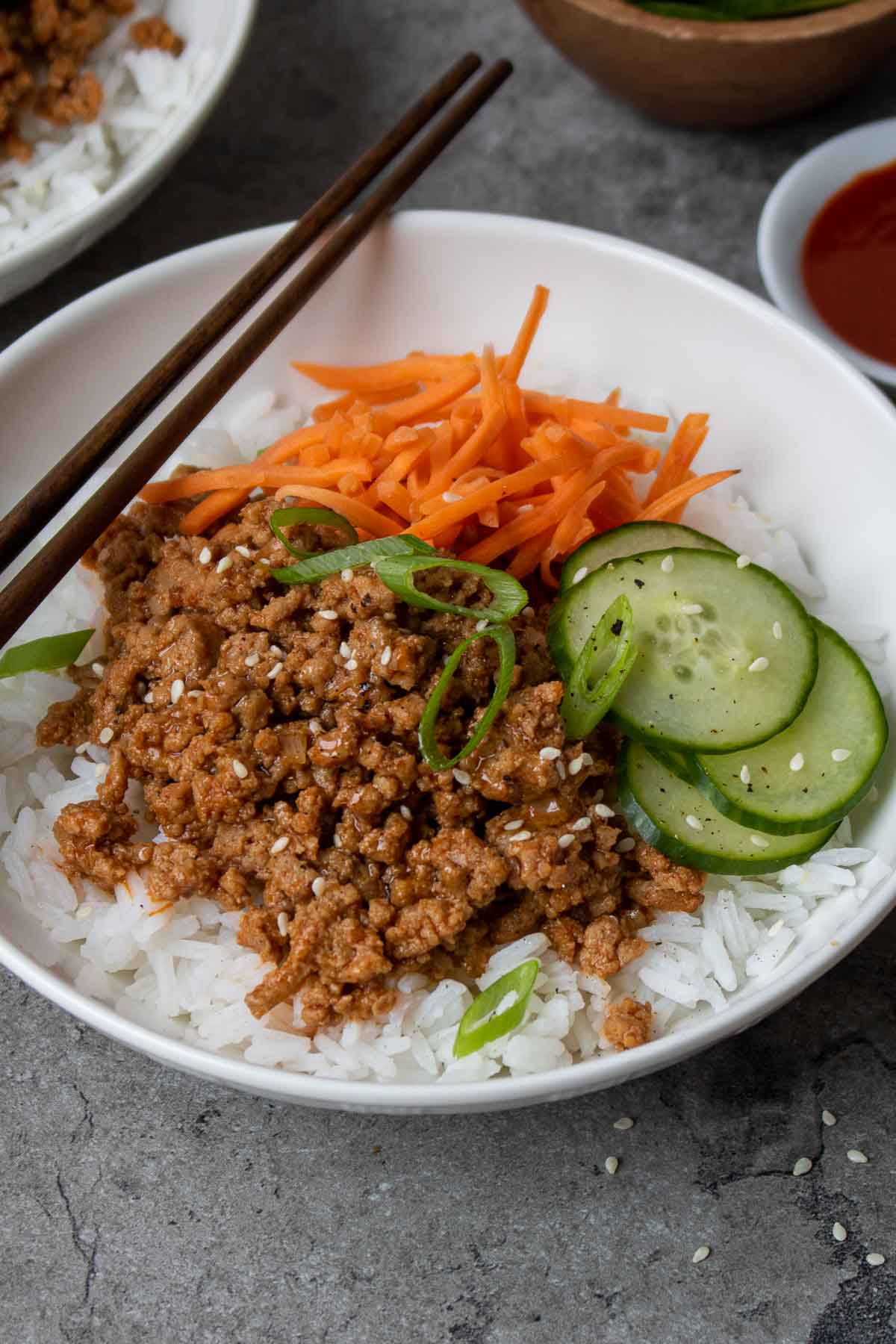 Ground turkey rice bowls with Korean sauce, cucumber, carrots, green onion, and sesame seed with chopsticks.
