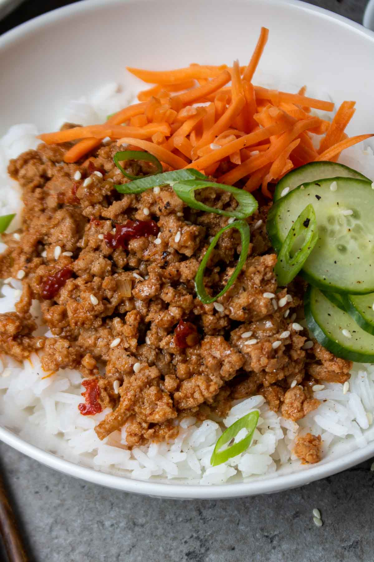 Closeup of a Korean ground turkey rice bowl with gochujang, sesame seeds, green onion, sliced cucumber, and shredded carrots.