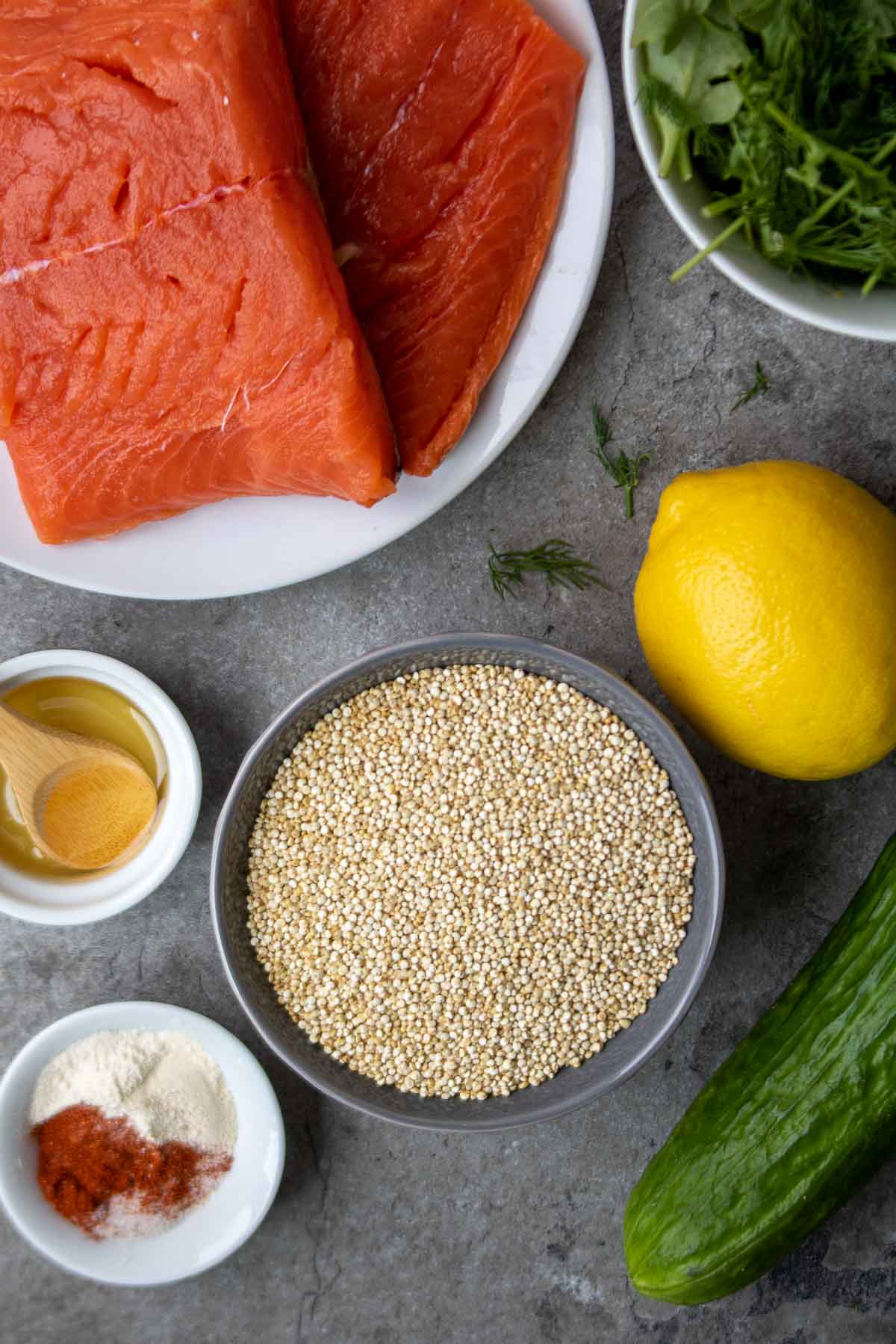 Ingredients for salmon and quinoa bowls, including salmon fillets, quinoa, cucumber, arugula, dill, lemon, and spices.