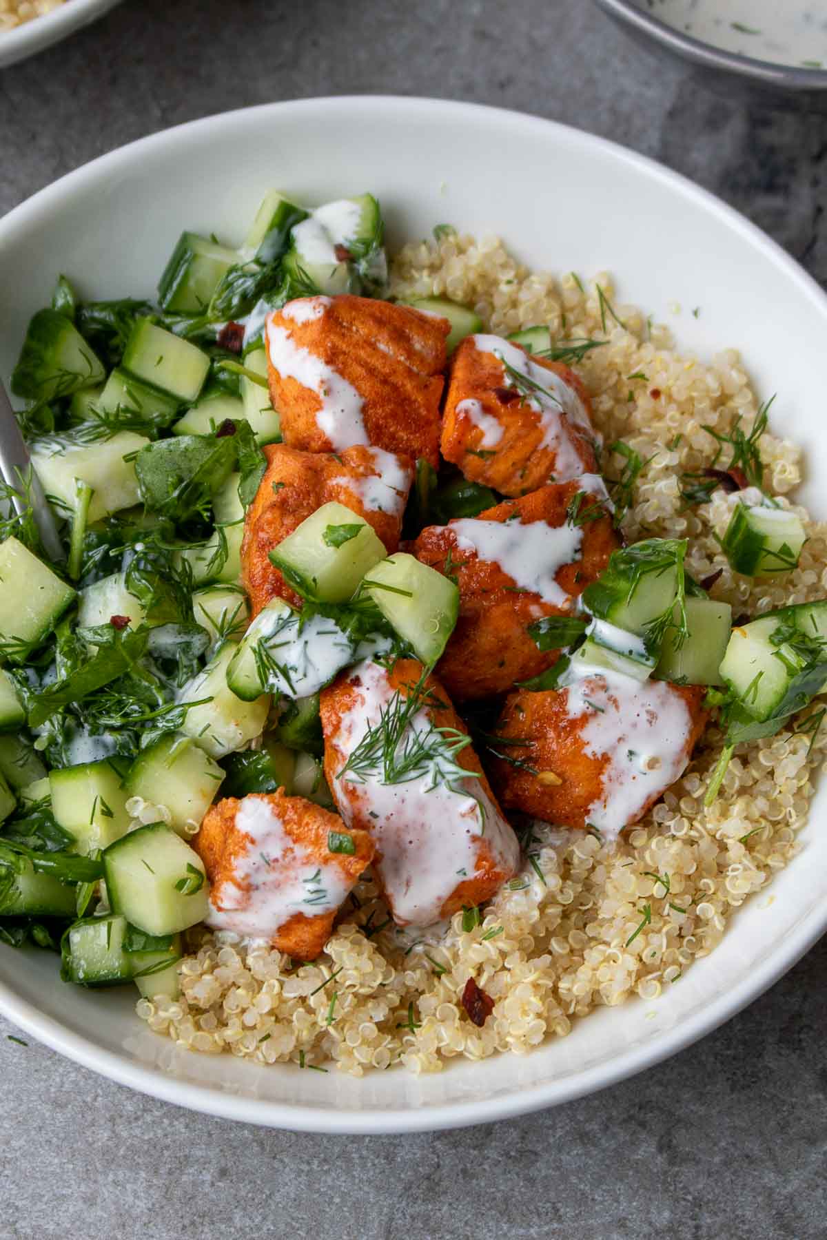 Baked salmon and quinoa bowl with cucumber salad and dressing.