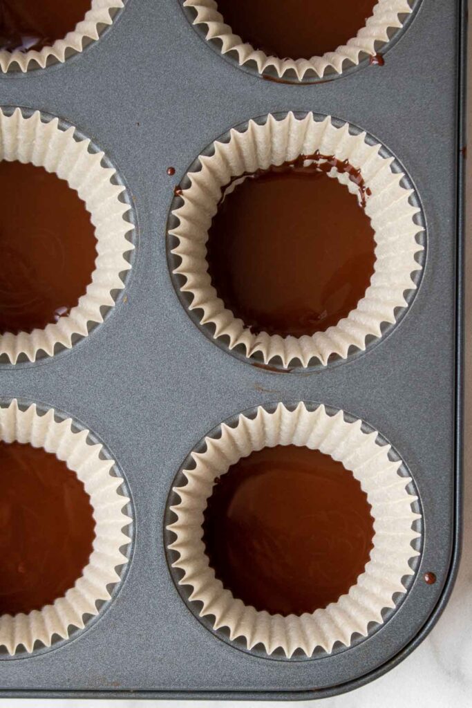 Muffin liners inside a muffin tin filled with melted dark chocolate