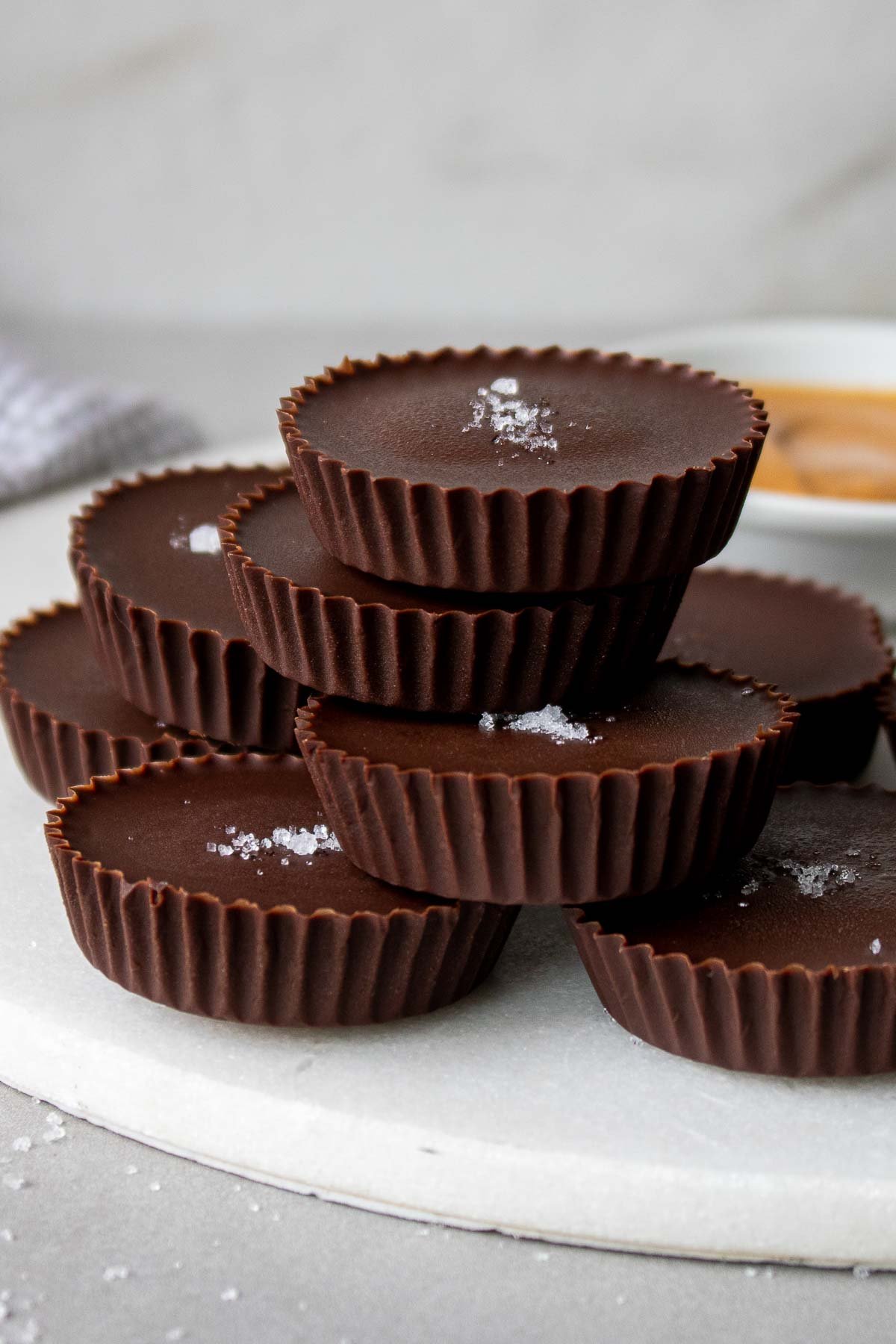 Dark chocolate peanut butter cups stacked on a plate with a sprinkling of flaky sea salt