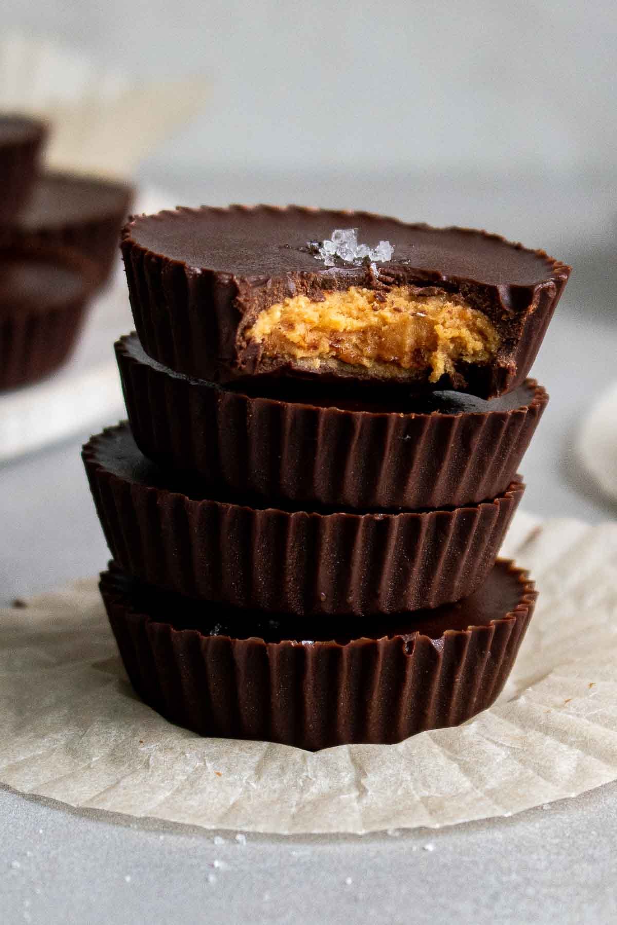 Dark chocolate peanut butter cups stacked with a bite taken and a sprinkle of sea salt