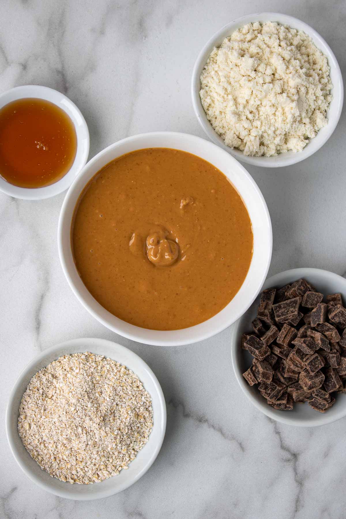 Ingrédients pour les barres protéinées : beurre d'arachide crémeux naturel, poudre protéinée à la vanille, farine d'avoine, miel et pépites de chocolat noir.