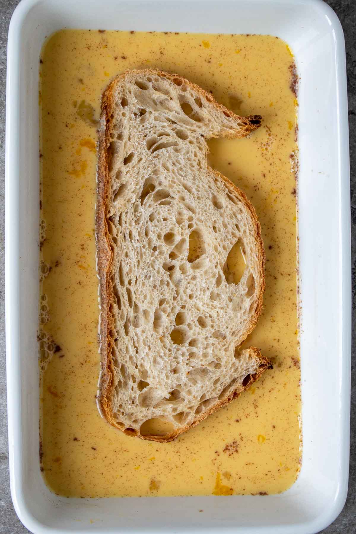 Slice of sourdough bread soaking in batter for French toast