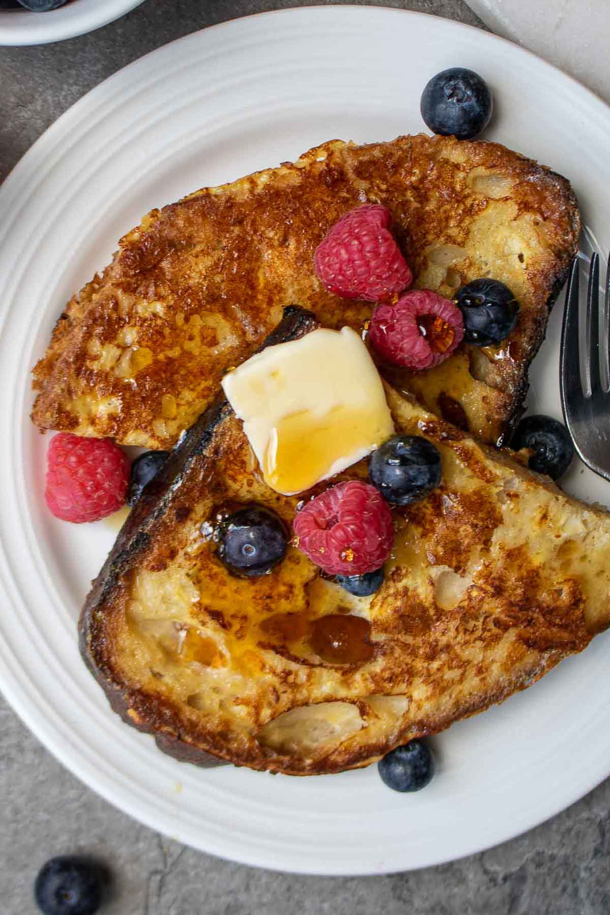 Close up images of slices of sourdough bread French toast with butter, berries, and syrup