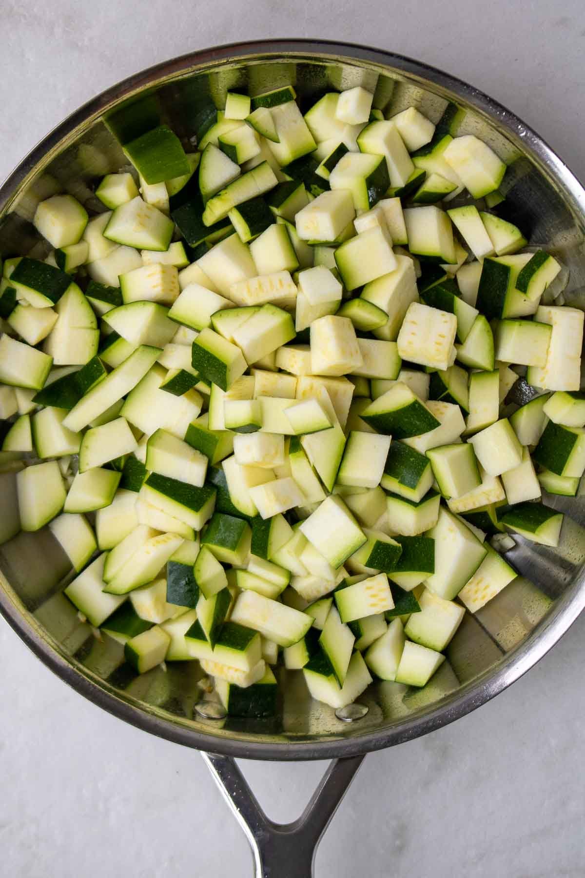 Raw diced zucchini in a pan with onion and garlic.