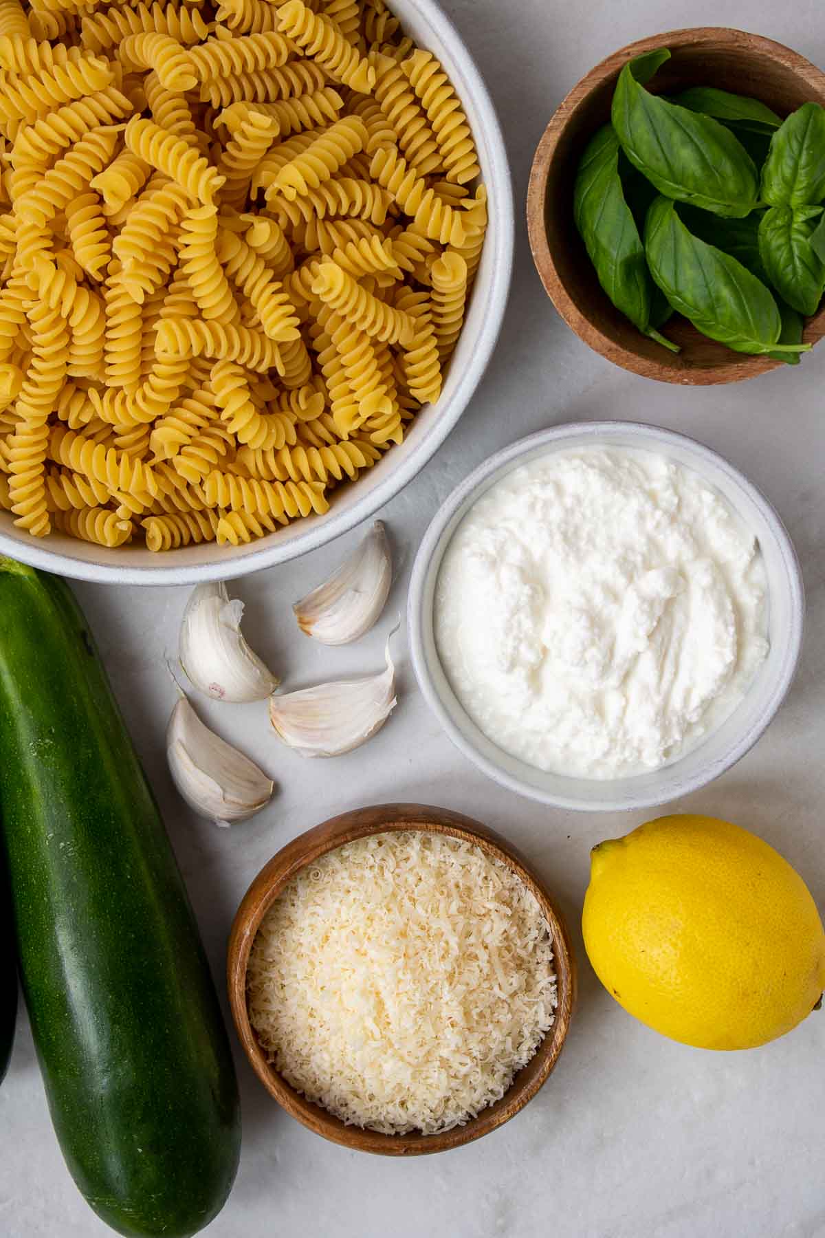 Ingredients for creamy zucchini pasta recipe: fusilli pasta, ricotta cheese, zucchini, garlic, parmesan cheese, lemon, and fresh basil.