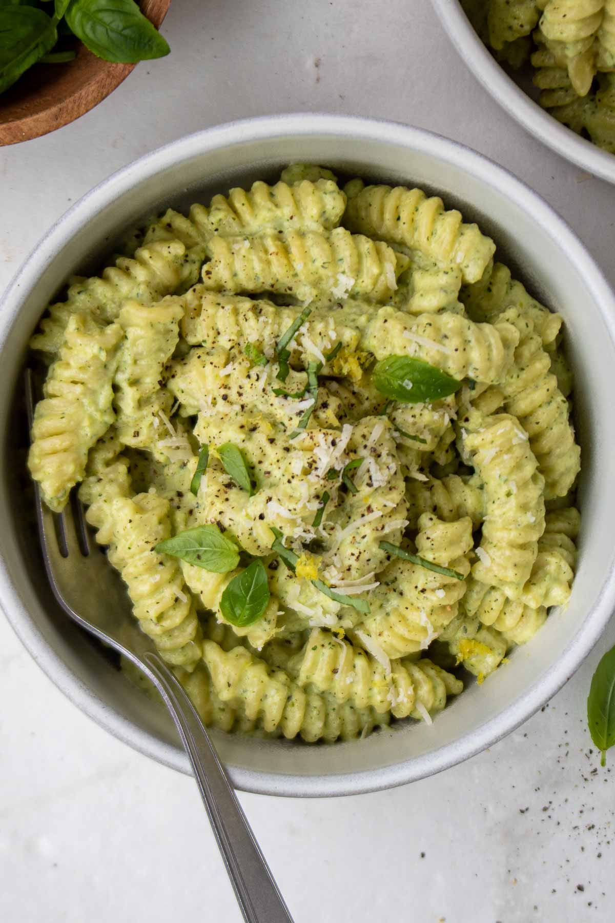 Creamy zucchini pasta in a white bowl with a fork with parmesan cheese and basil on top. 