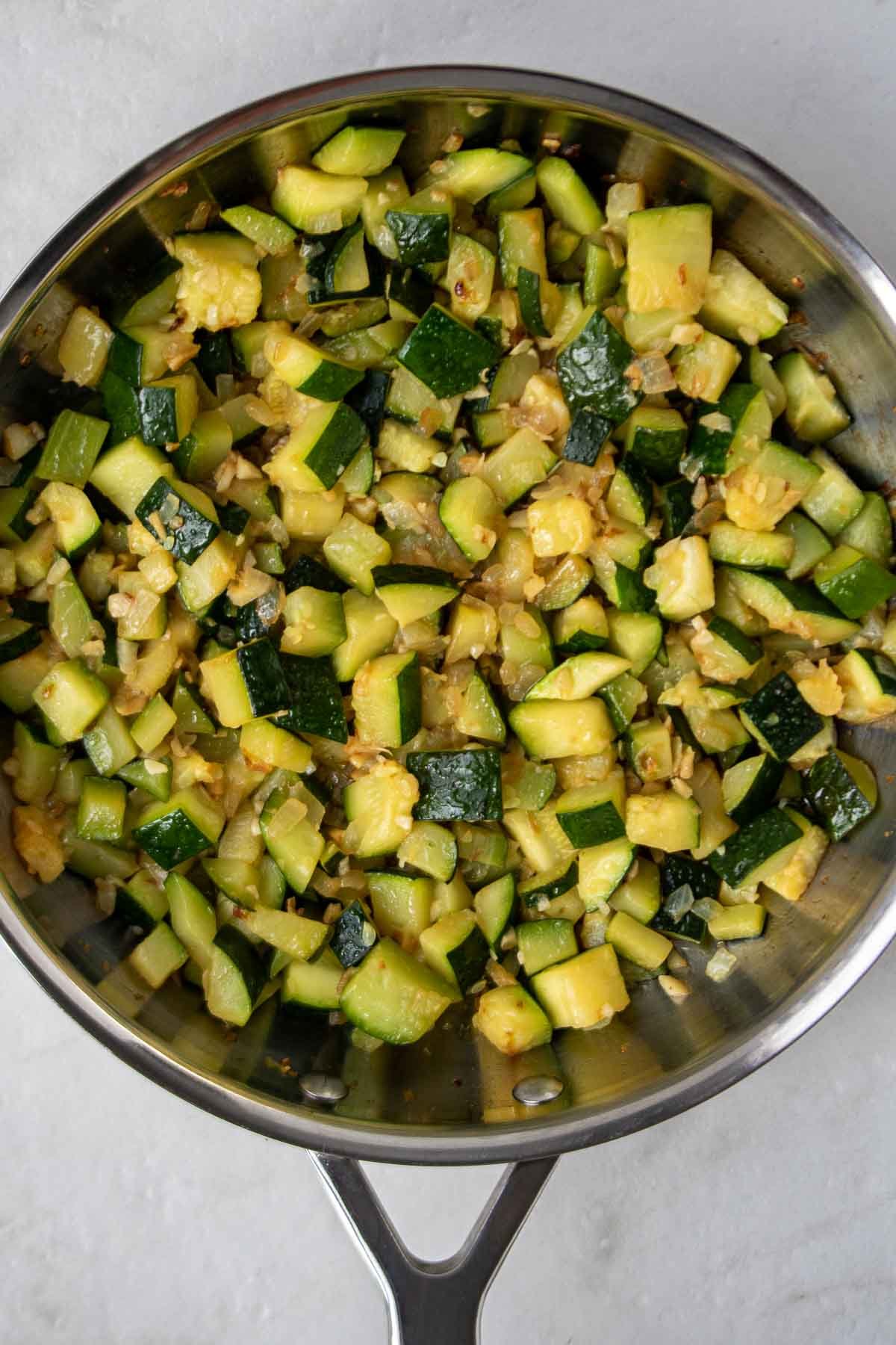 Cooked diced zucchini in a pan with onion and garlic.