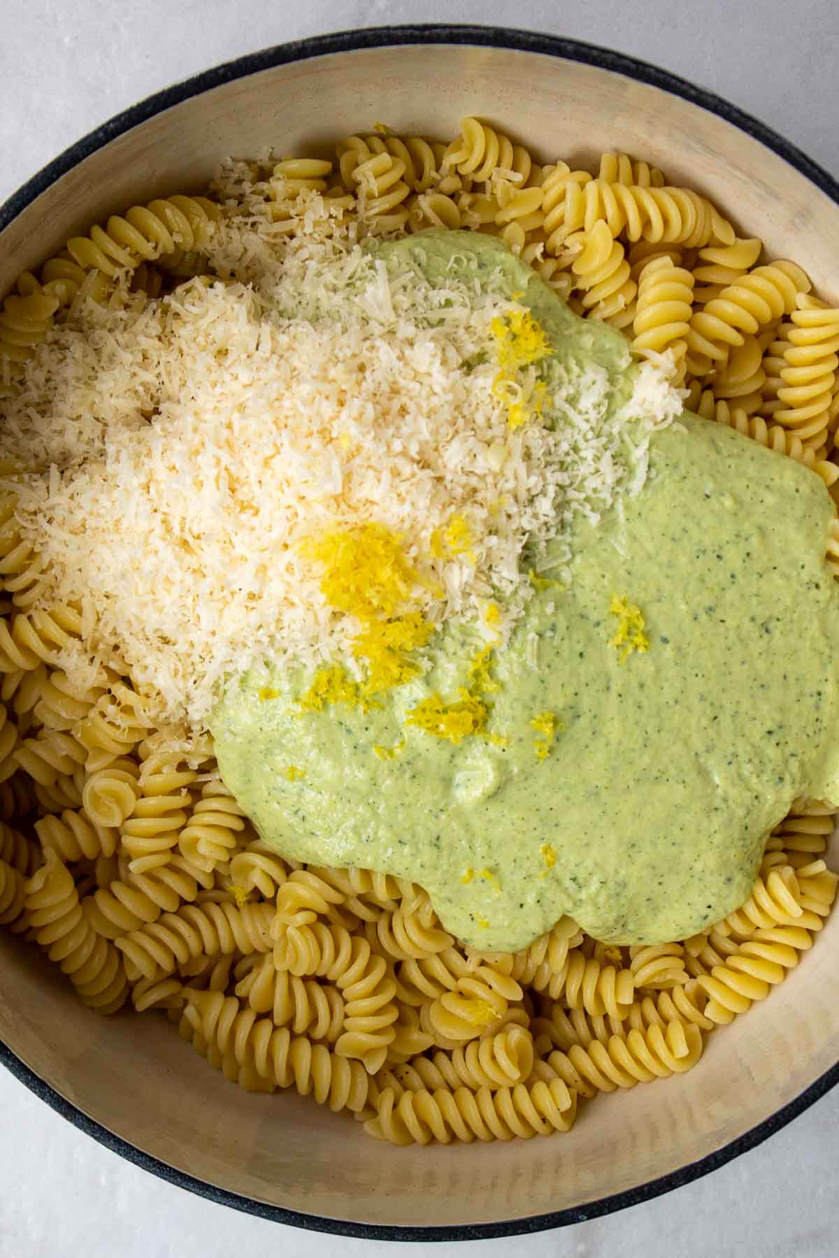 Fusili pasta, creamy zucchini pasta, shredded cheese, and lemon zest in a pot.