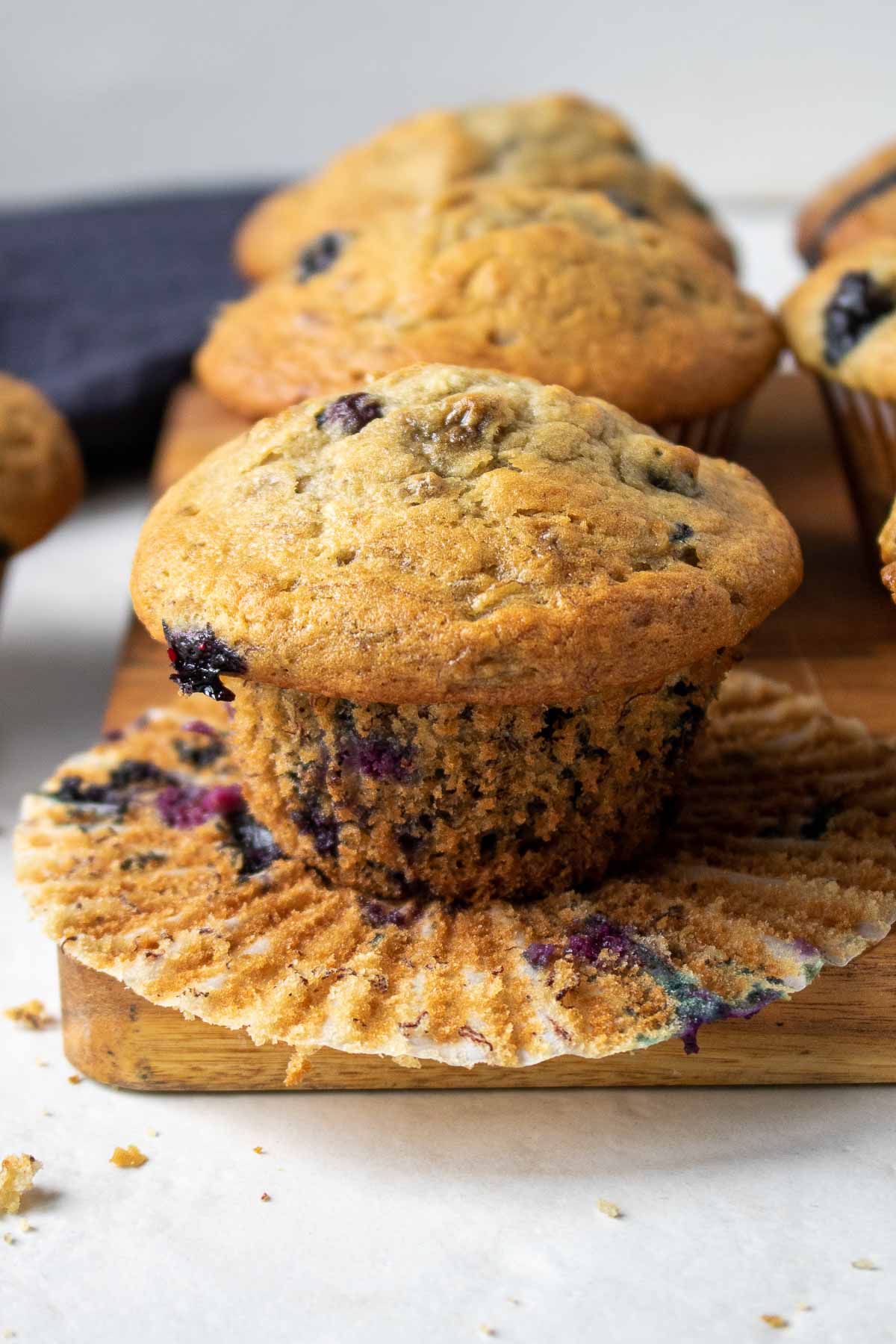 Healthy banana blueberry muffins in an open muffin wrapper on a cutting board.
