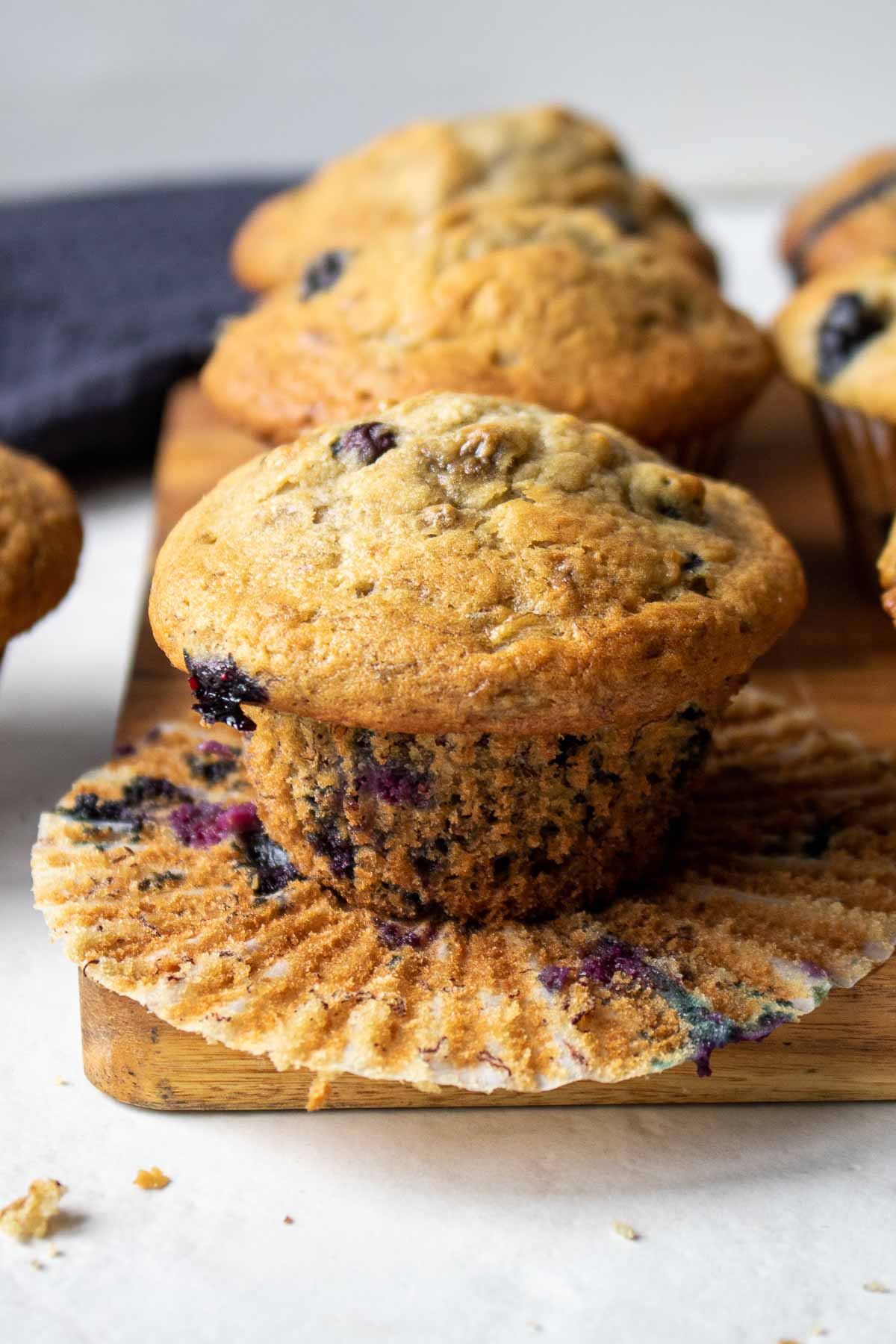 Blueberry banana muffins on a cutting board in an open muffin liner ready to eat