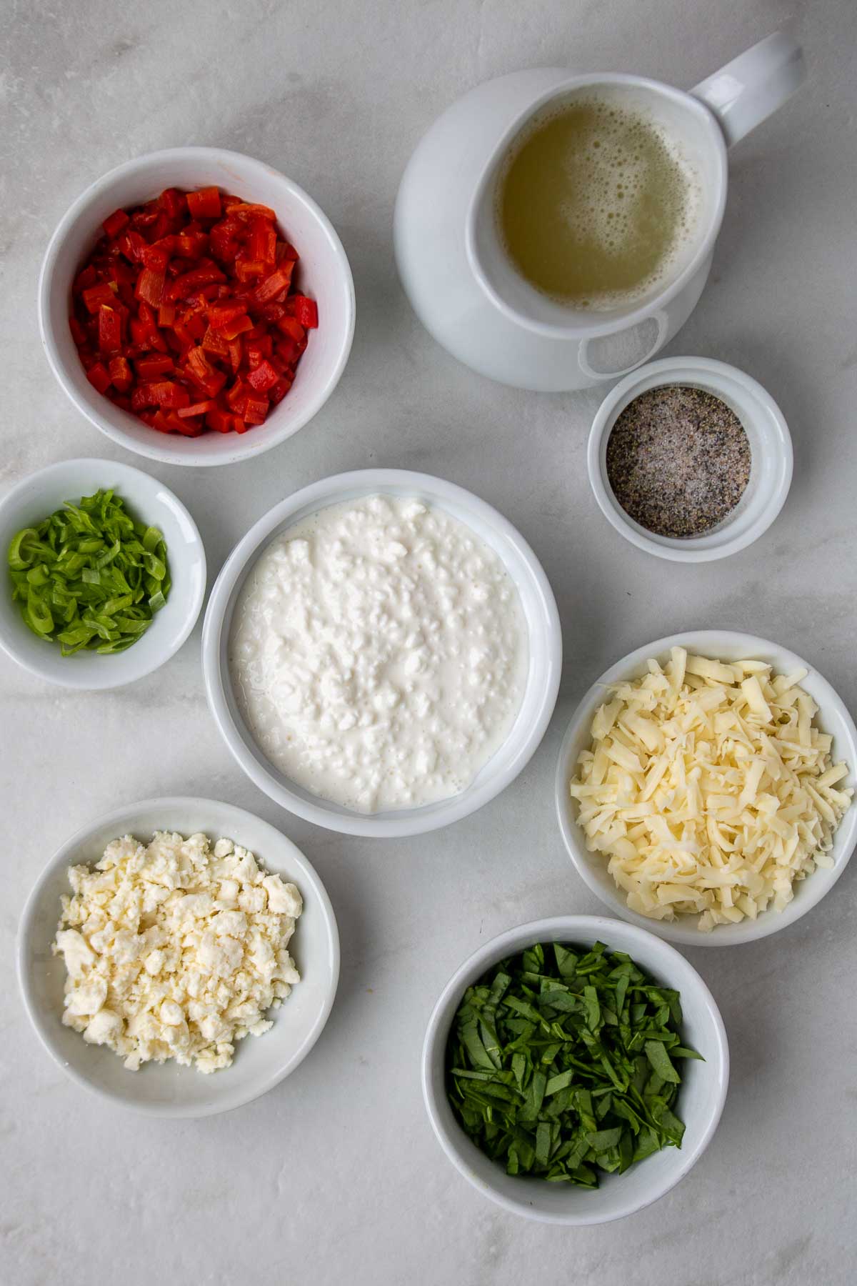 Ingredients for egg white bites: liquid egg whites, cottage cheese, shredded Monterey jack cheese, feta cheese, green onion, spinach, roasted red peppers, cornstarch, salt, and pepper.
