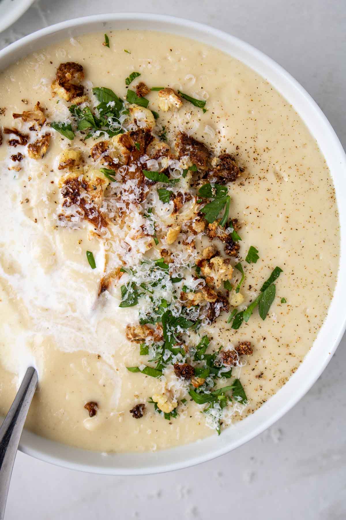 Close up of roasted cauliflower soup in a bowl with roasted florets, parley, milk, salt and black pepper