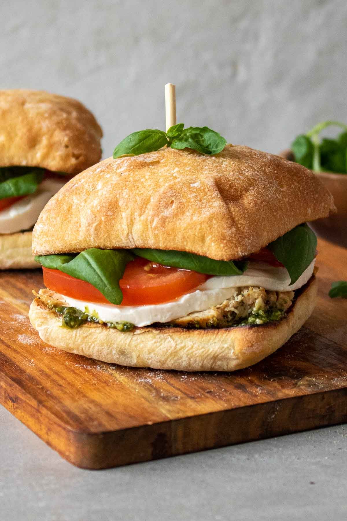 Chicken caprese sandwich on a wood cutting board with a toothpick and fresh basil on top