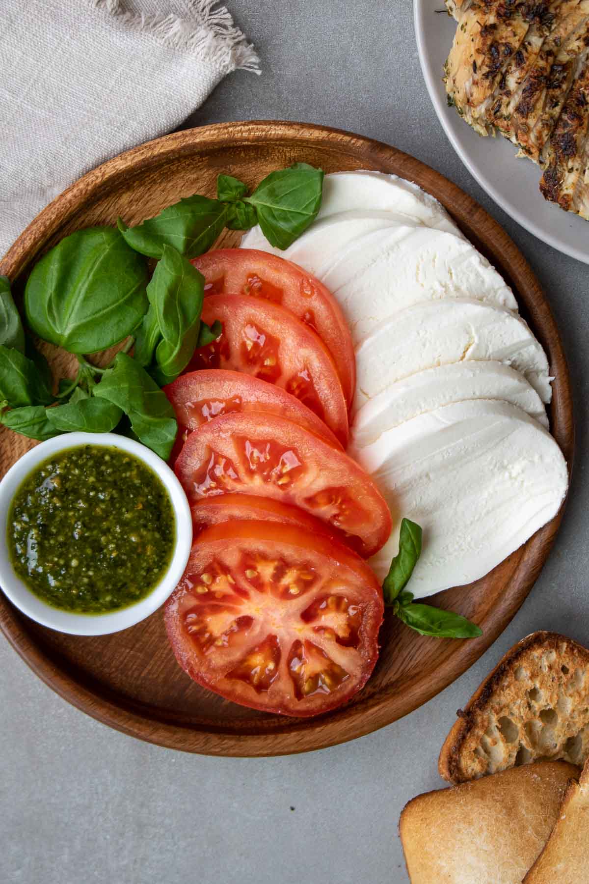 Ingredients for a chicken caprese sandwich; grilled chicken breasts, sliced mozzarella, sliced tomatoes, pesto, basil leaves, grilled ciabatta
