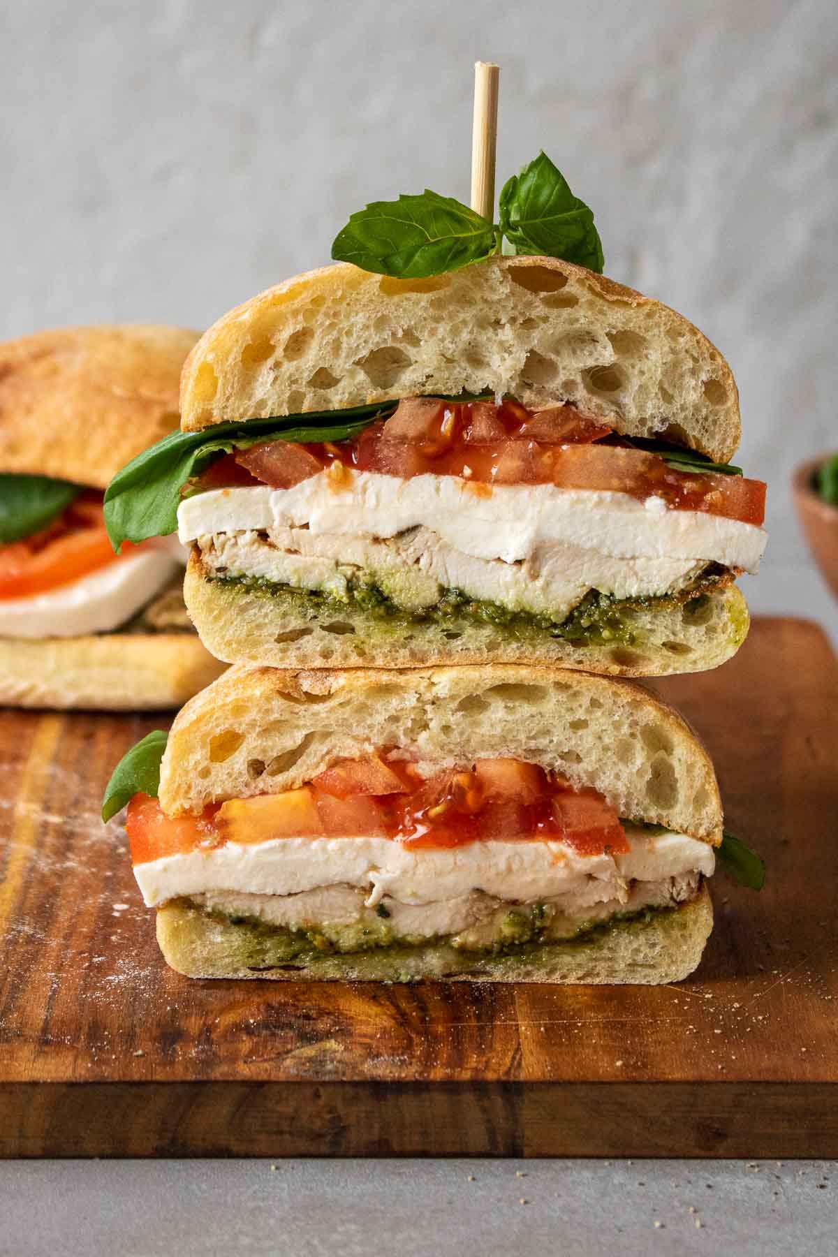 Chicken caprese sandwich cut in half and stacked on top of each other on a cutting board