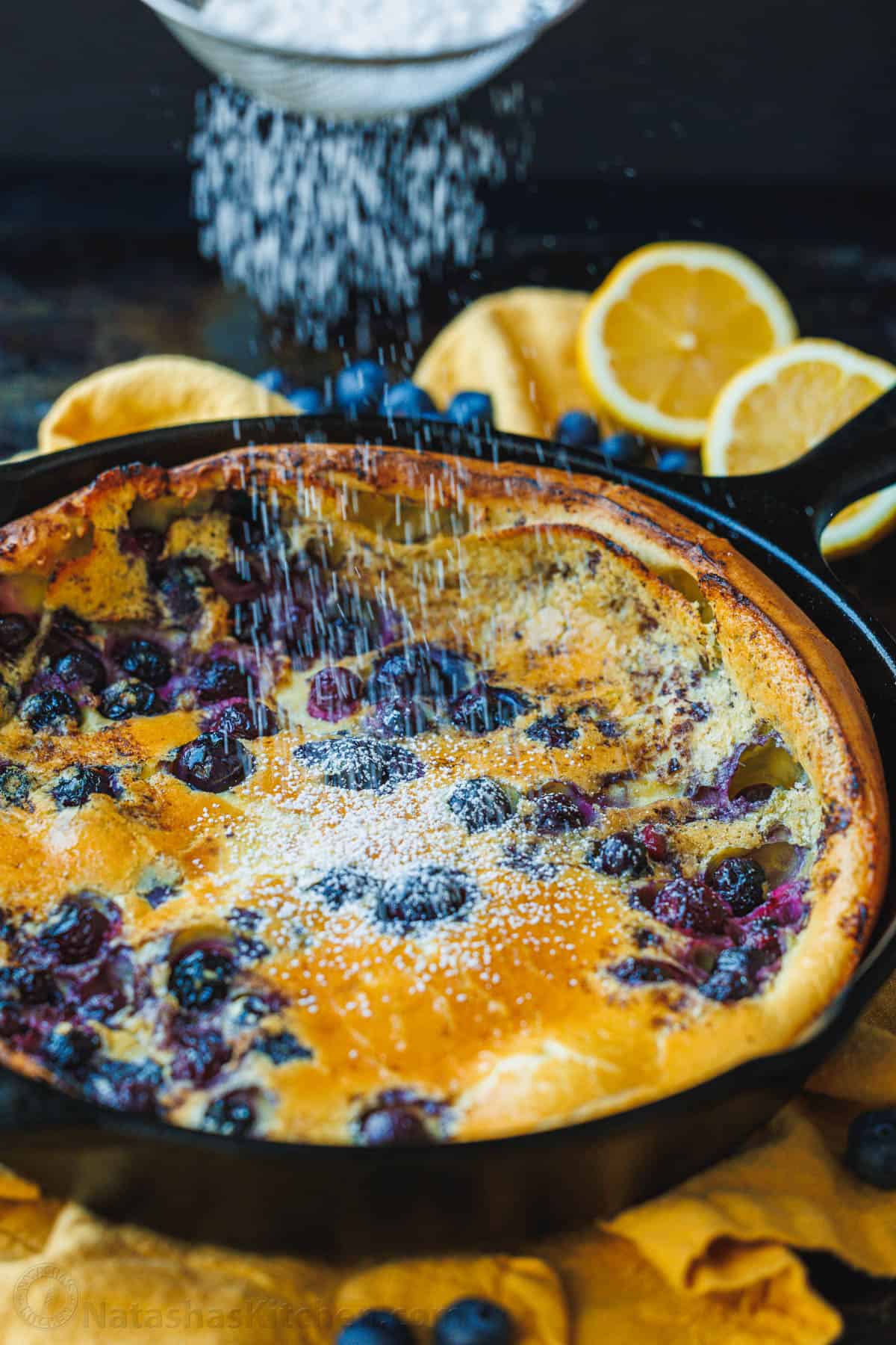 dutch baby baked with fruit in skillet with powdered sugar sprinkled on top