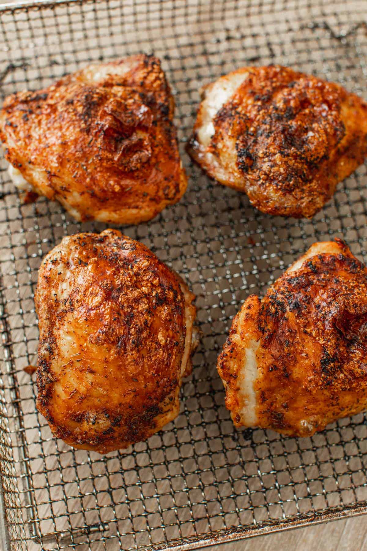 Four cooked air fryer chicken thighs in the air fryer basket.