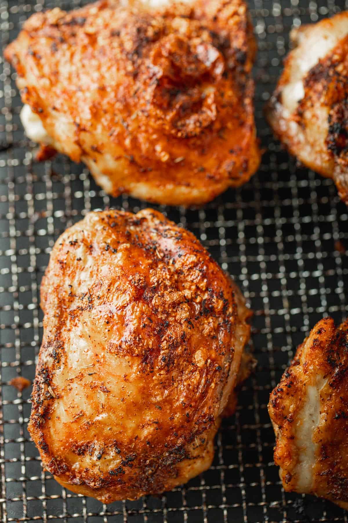 Close up of four cooked air fryer chicken thighs in the air fryer basket.