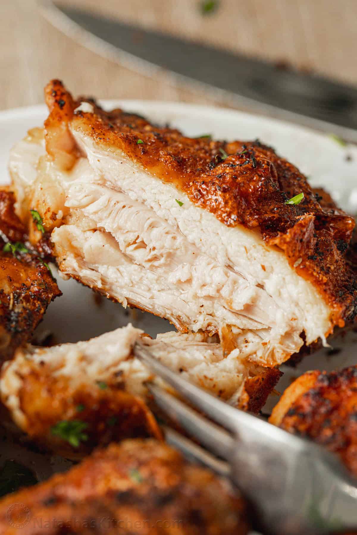 A forkful of cooked chicken thigh cut away from the rest of the thigh on a plate.