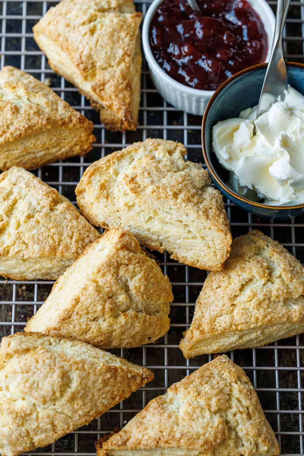 Classic scones on a wire cooling rack with clotted cream and jam in ramekin dishes to use as toppings