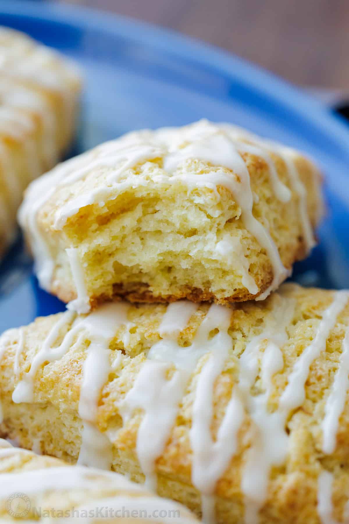 Flaky, soft textured scones on a plate, drizzled with vanilla glaze.
