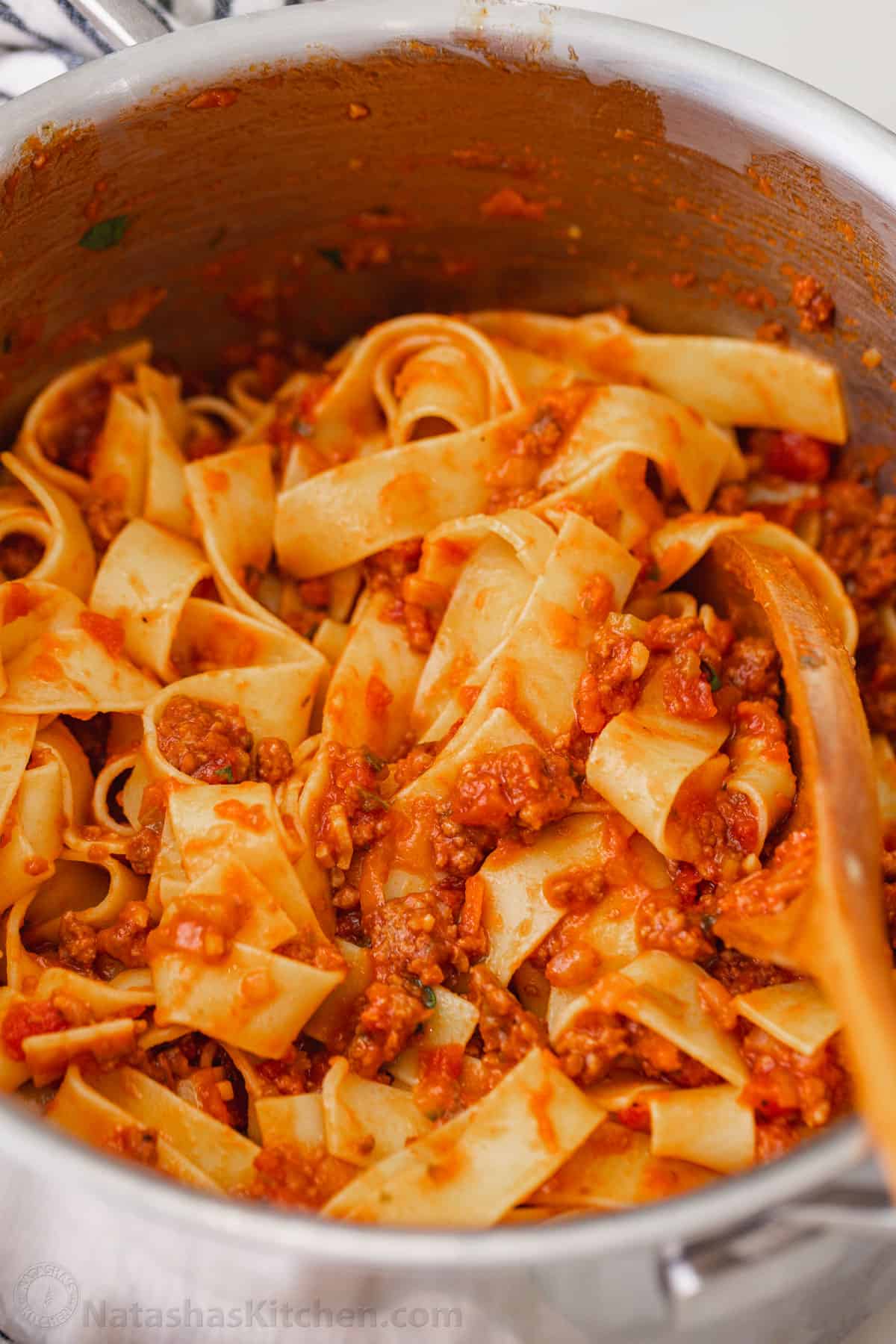 A large pot of pappardelle pasta bolognese, with a wooden spoon.
