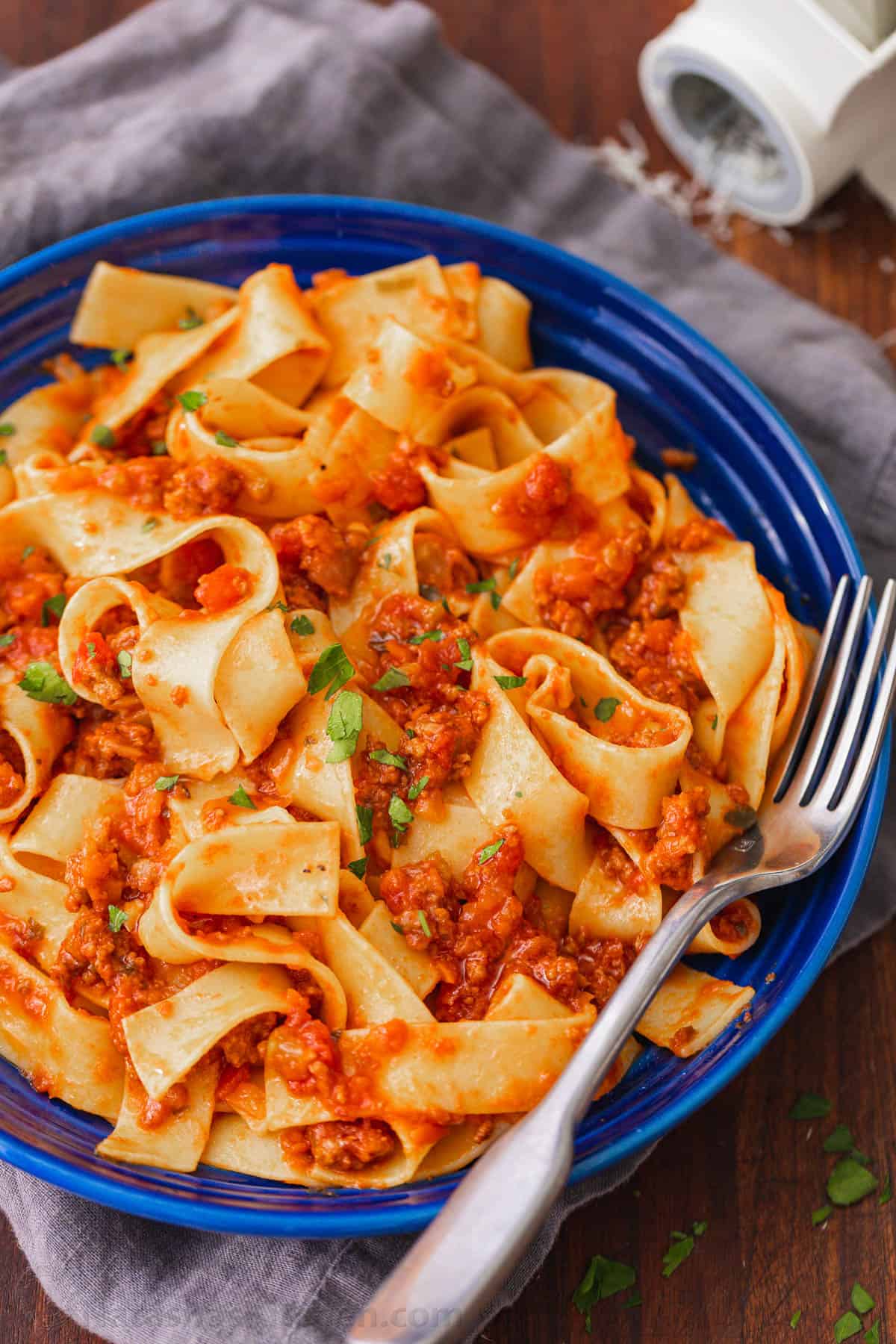 Pappardelle pasta with bolognese sauce in a blue bowl, with a fork.