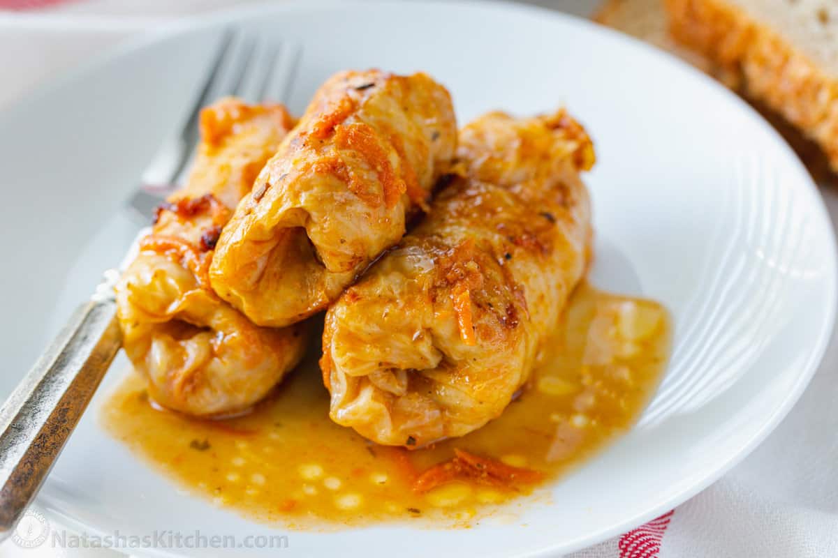 Three cabbage rolls served on a white plate next to a fork.